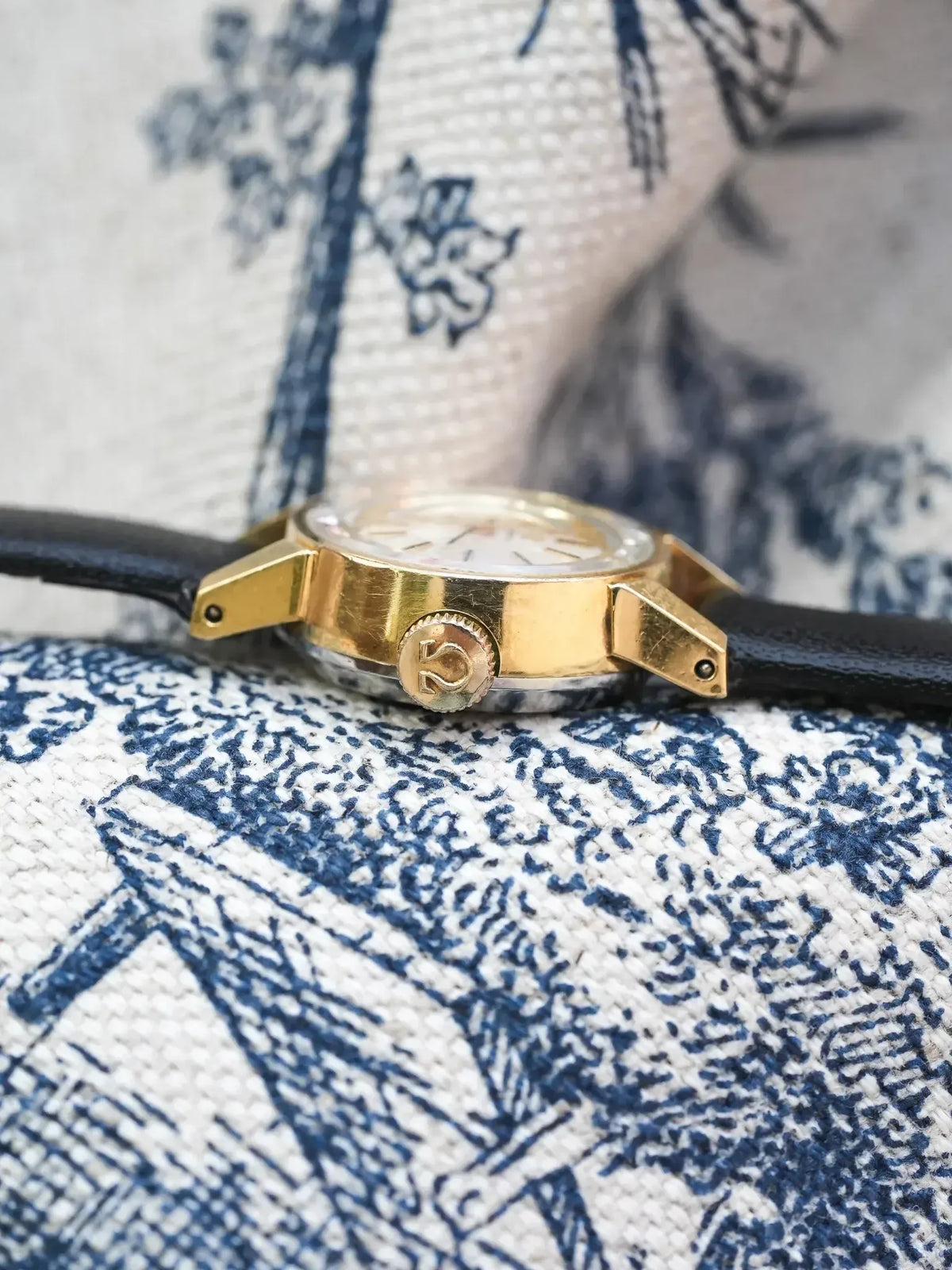 Omega vintage watch with gold case, black leather strap, on patterned fabric