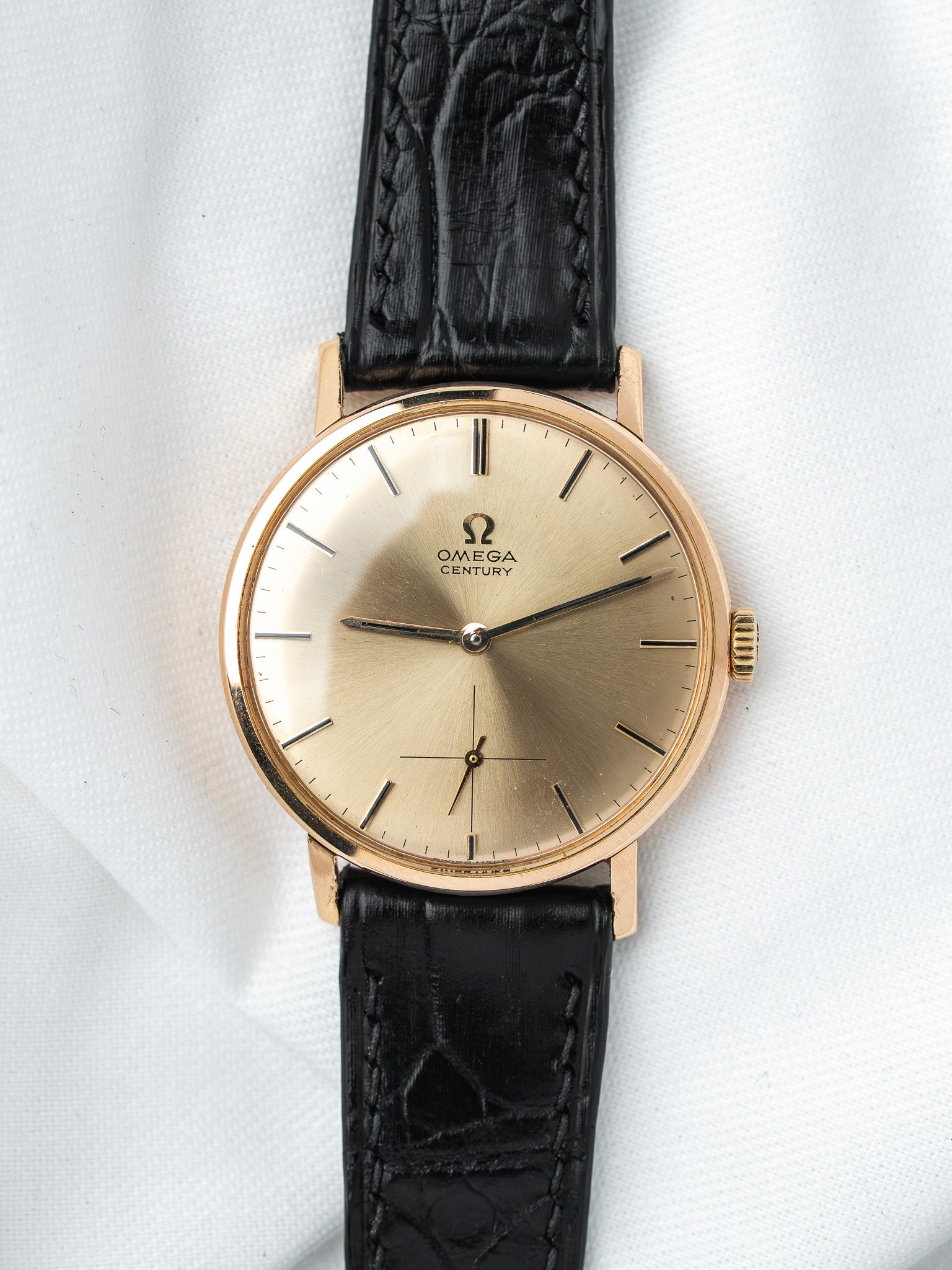 Vintage Omega Century watch with gold case, cream dial, black leather strap on white background