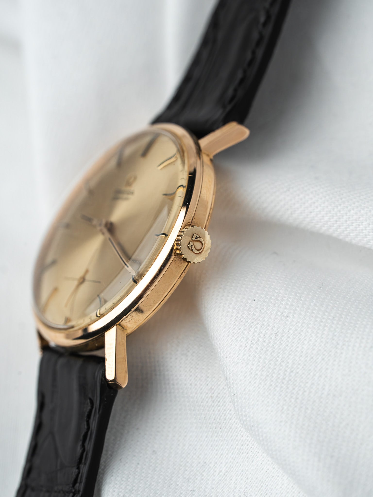 Vintage Omega watch with gold case, cream dial, black leather strap on white fabric