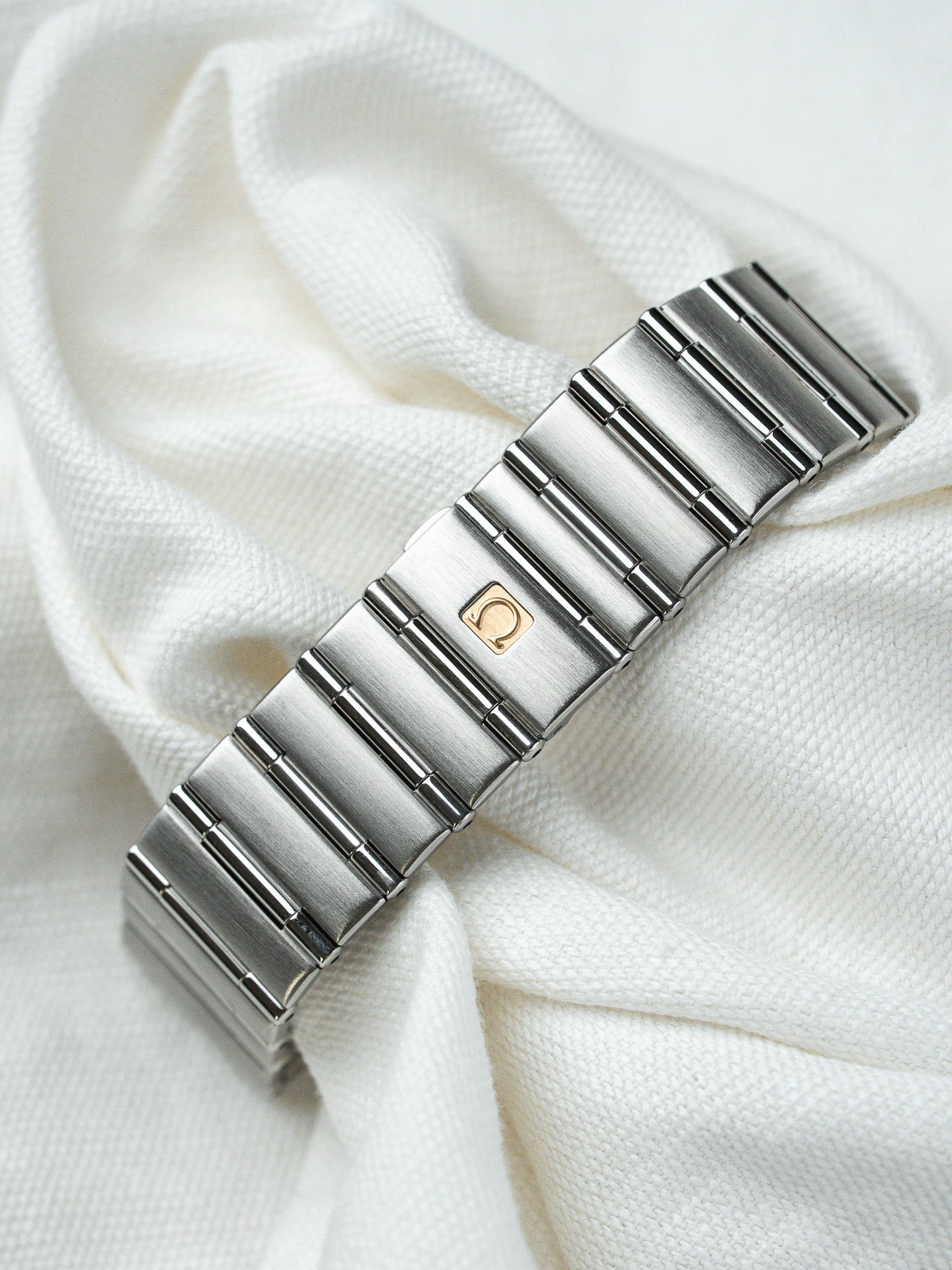 Omega vintage bracelet in stainless steel with gold logo on white fabric