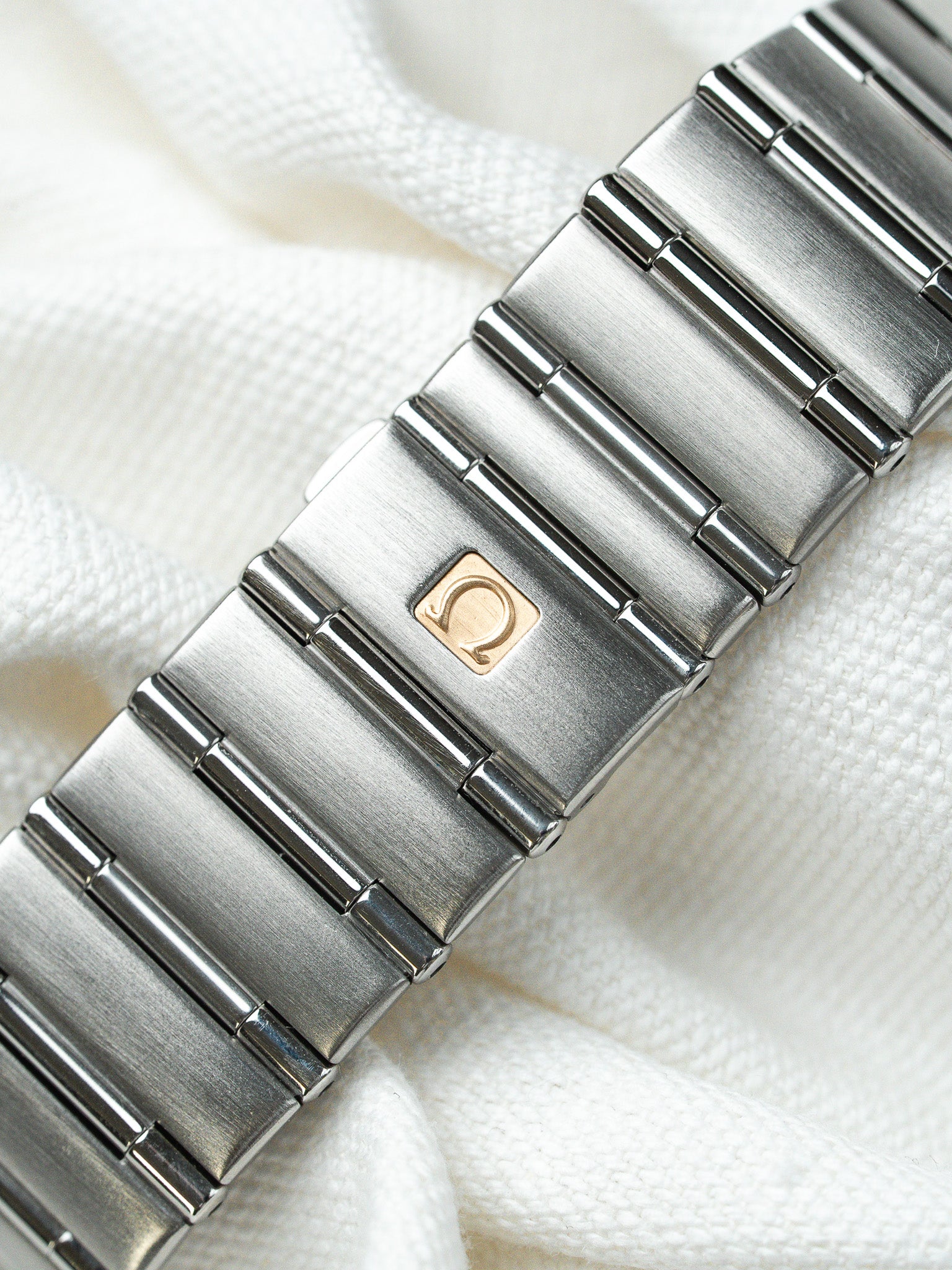 Omega vintage watch bracelet in brushed steel with gold logo on white fabric