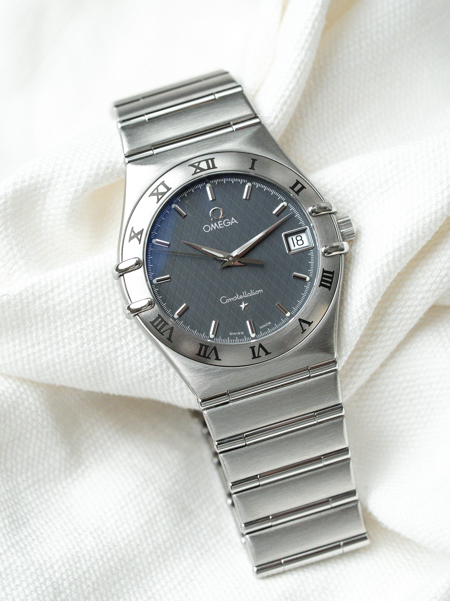 Omega Constellation vintage watch with blue dial, Roman numerals, steel bracelet on white fabric