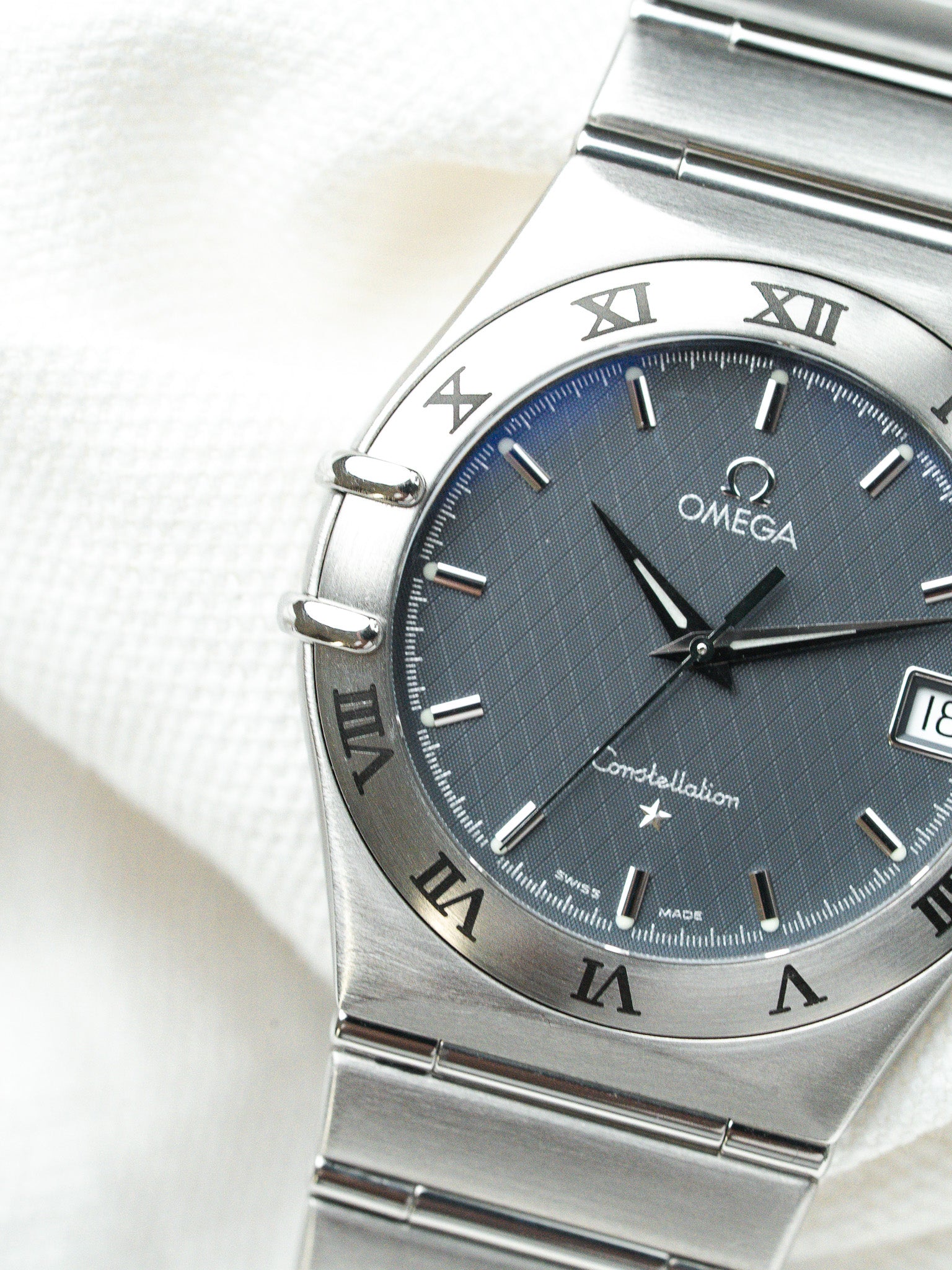 Omega Constellation watch with blue dial, Roman numerals, steel bracelet on white fabric