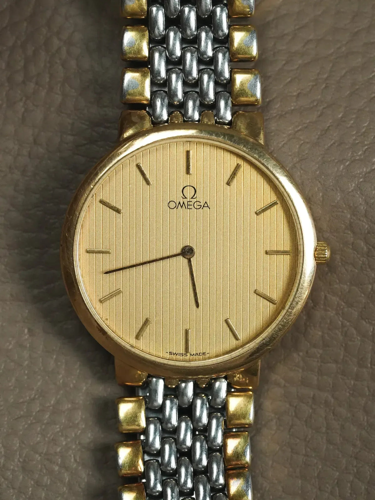 Omega vintage watch with gold dial, two-tone bracelet, on textured surface