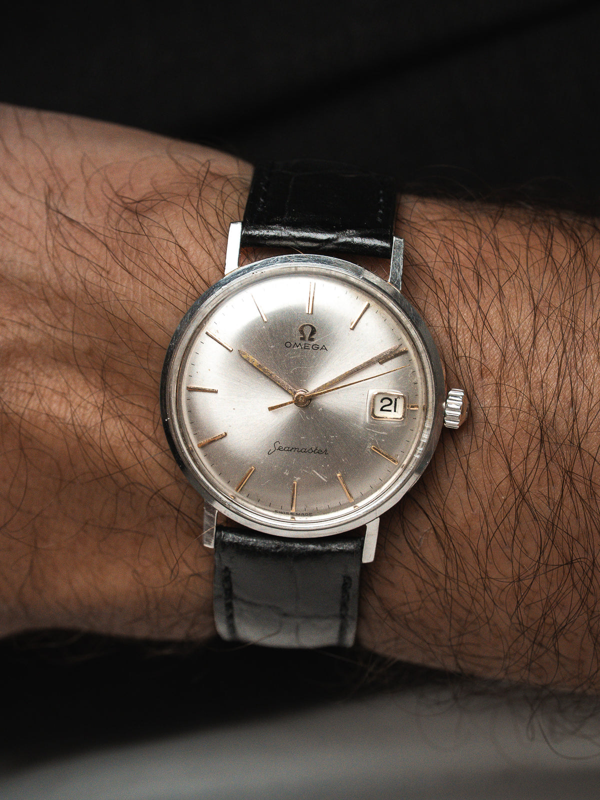 Montre Omega Seamaster vintage, cadran argenté et bracelet cuir noir, portée au poignet