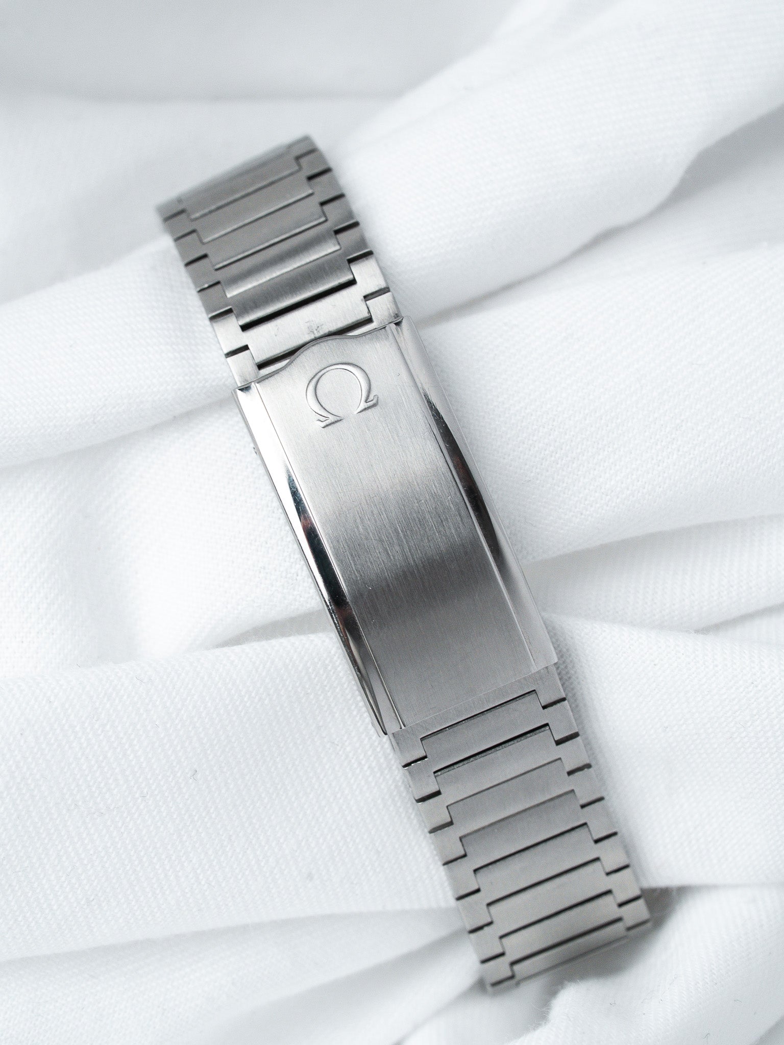 Omega vintage watch bracelet in brushed steel with logo clasp on white fabric