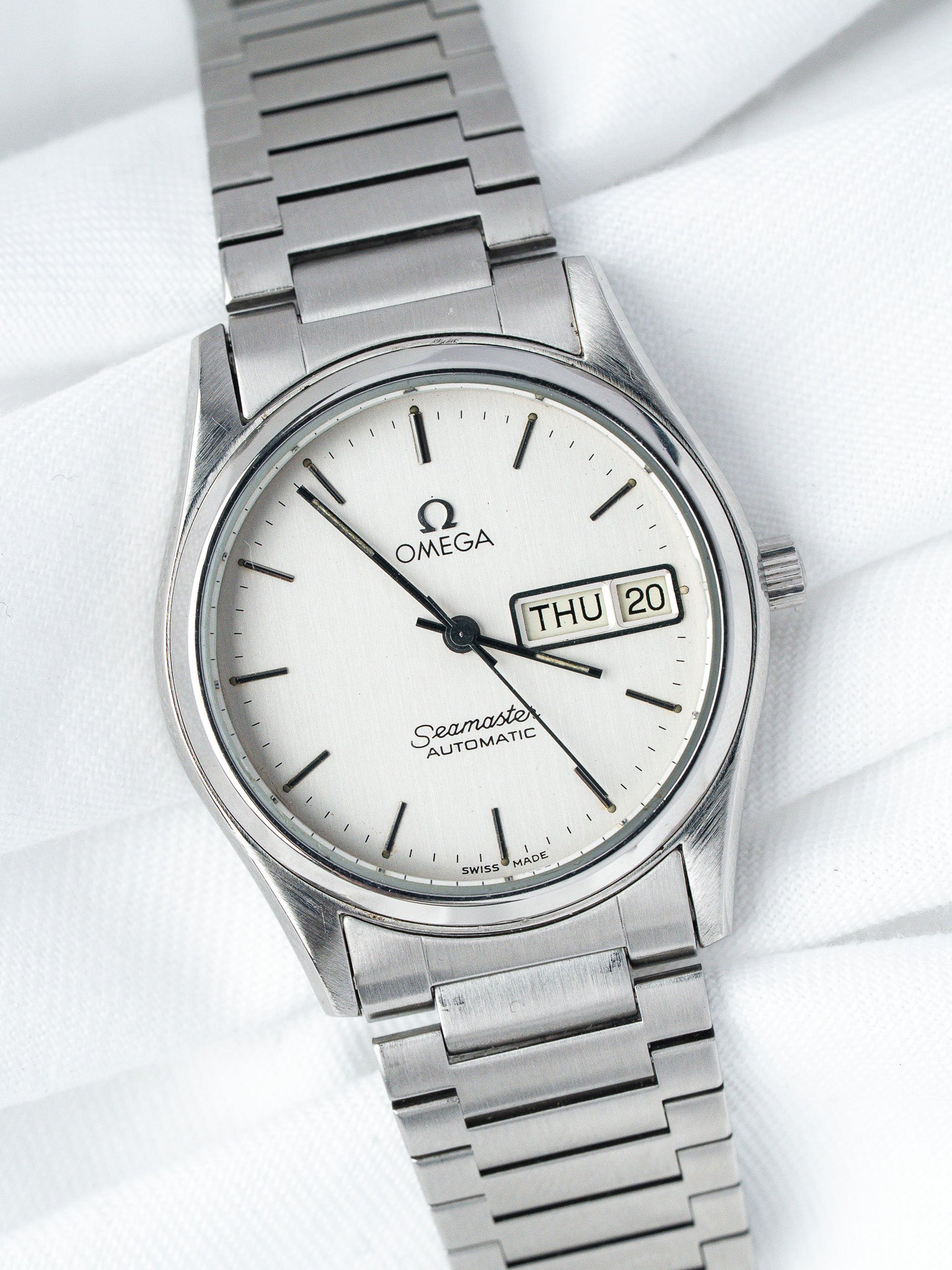 Omega Seamaster vintage automatic watch with white dial, day-date, and steel bracelet on white fabric