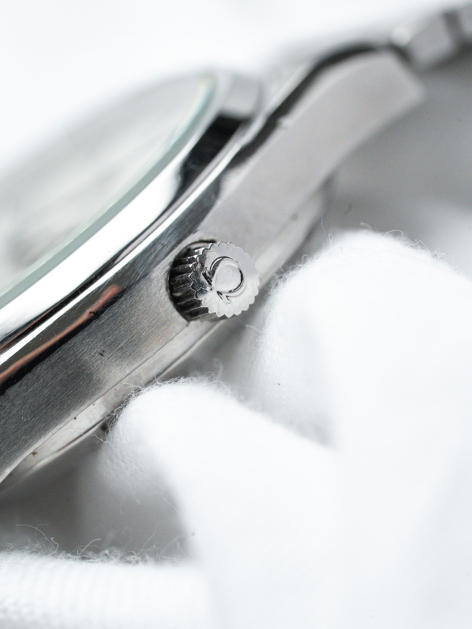 Omega vintage watch crown detail on brushed steel case, resting on white fabric