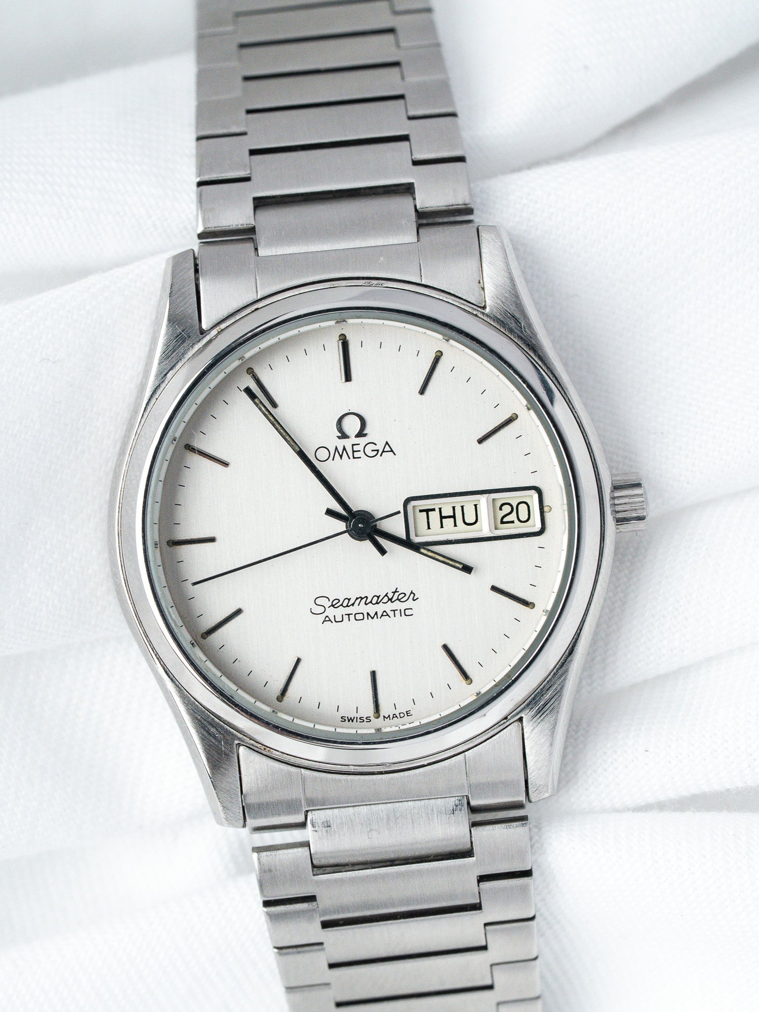Omega Seamaster vintage automatic watch with white dial, day-date, and steel bracelet on white fabric