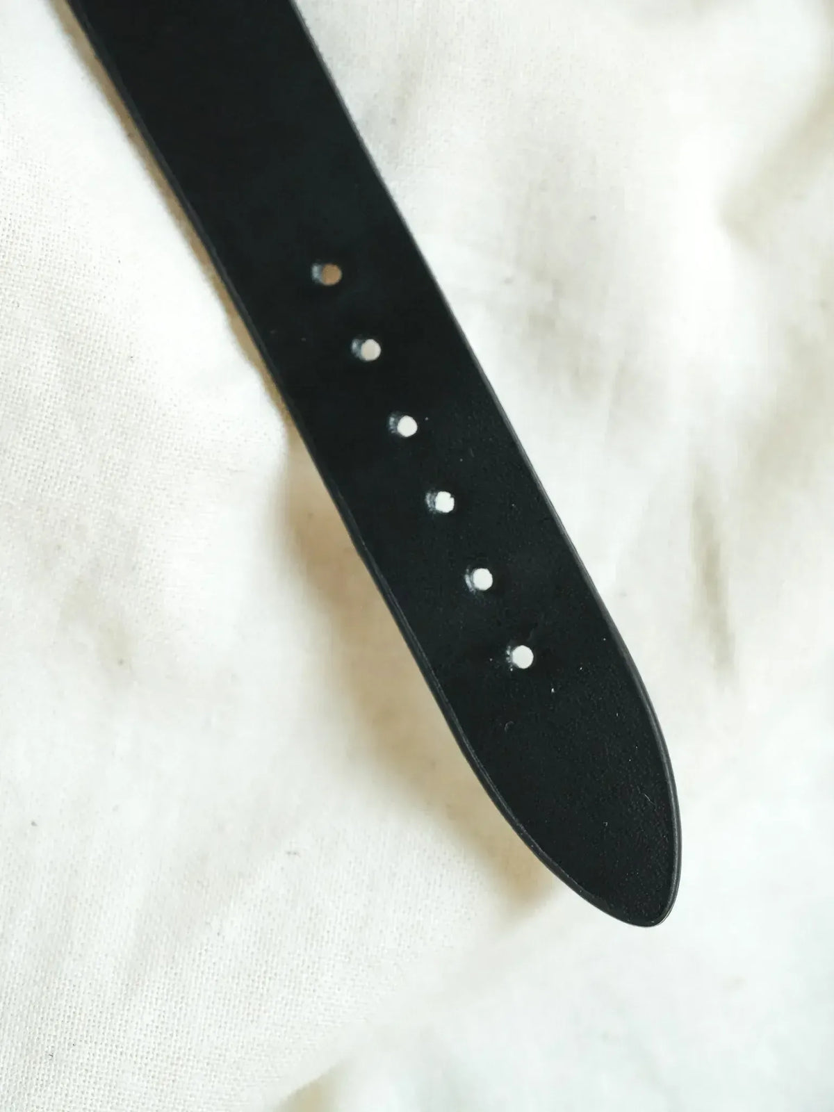 Black leather watch strap with white stitching, laid on white fabric background