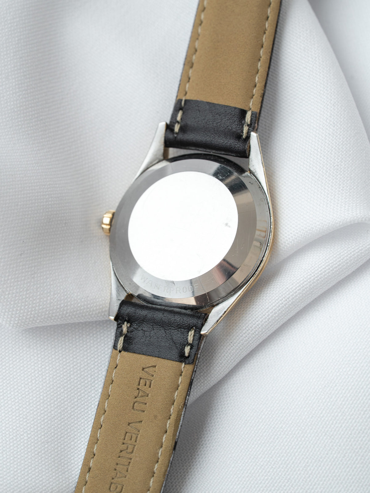 Vintage watch with stainless steel case, black leather strap, and waterproof engraving on back