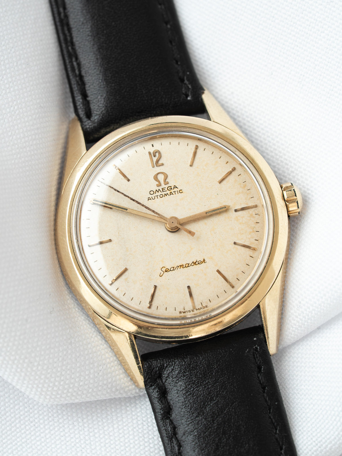 Vintage Omega Seamaster watch with gold case, cream dial, and black leather strap
