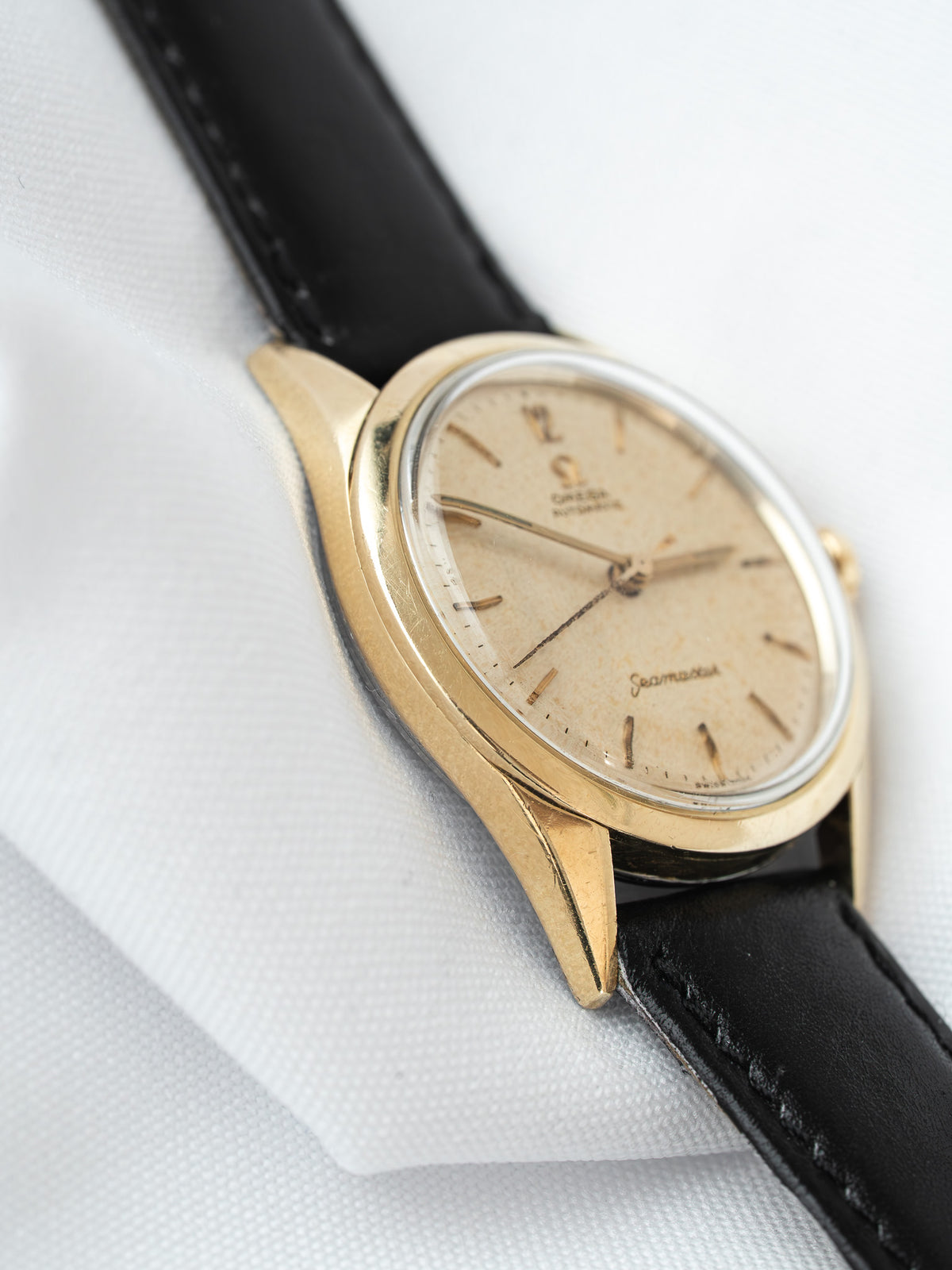 Omega Seamaster vintage watch with gold case, cream dial, black leather strap on white fabric