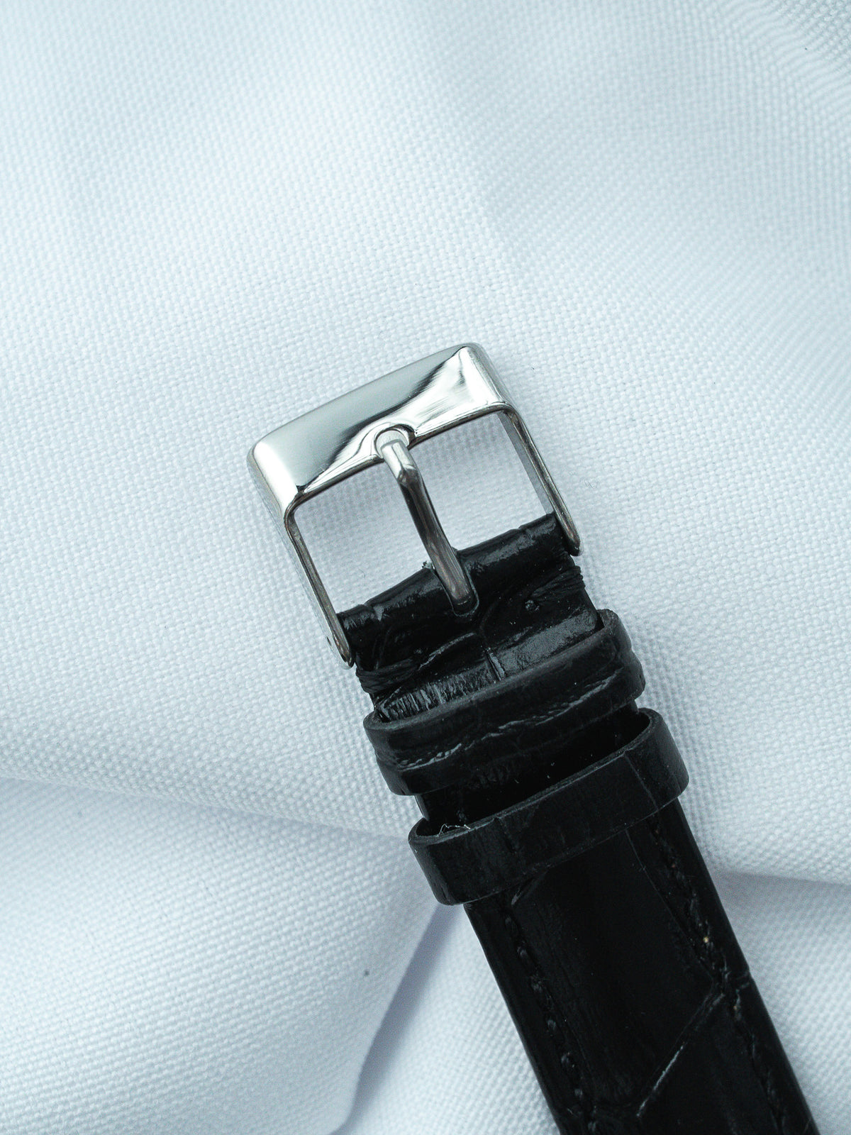 Black alligator leather watch strap with polished steel buckle on white fabric