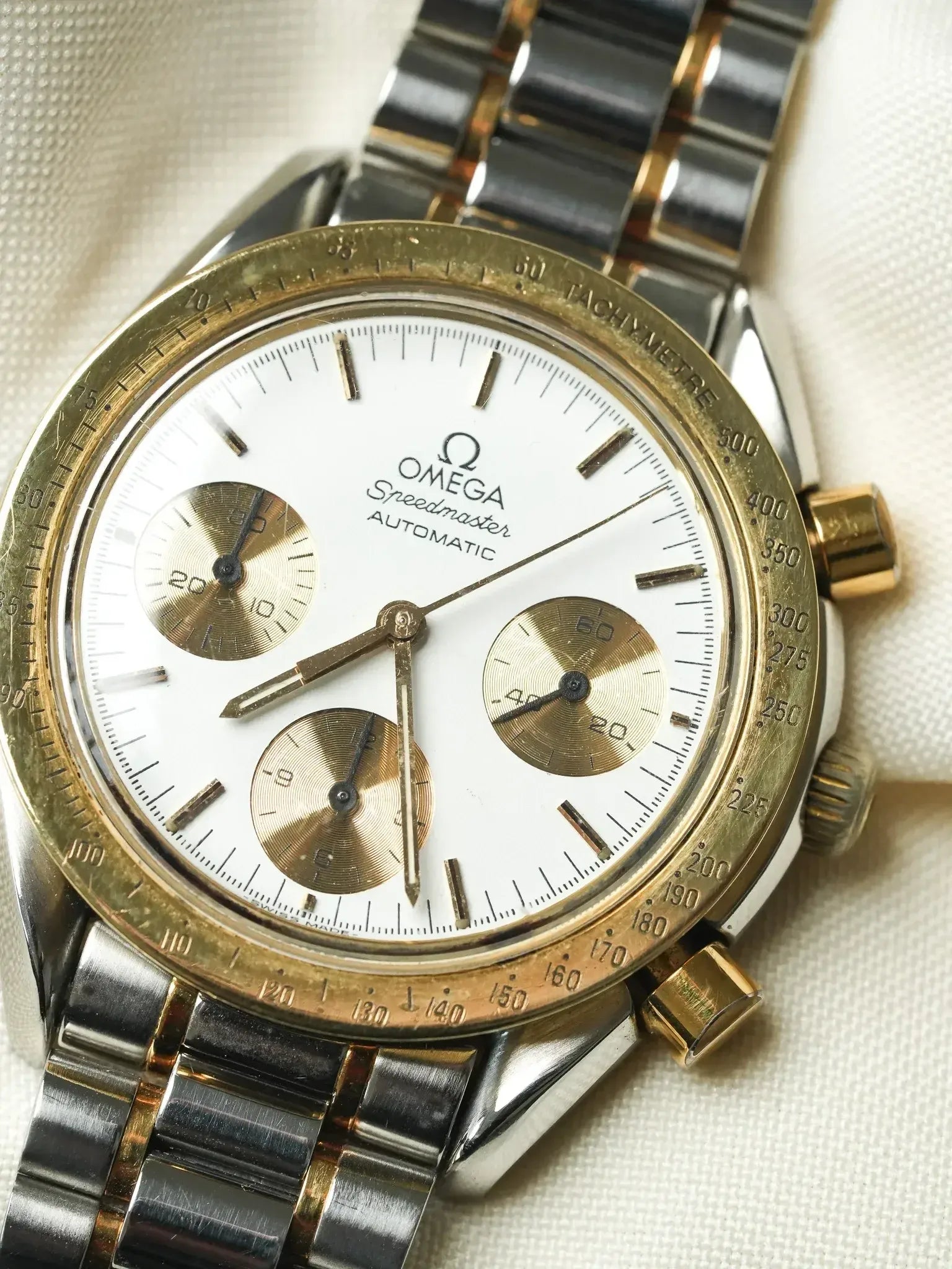 Vintage Omega Speedmaster Automatic chronograph with white dial, gold subdials, and two-tone bracelet