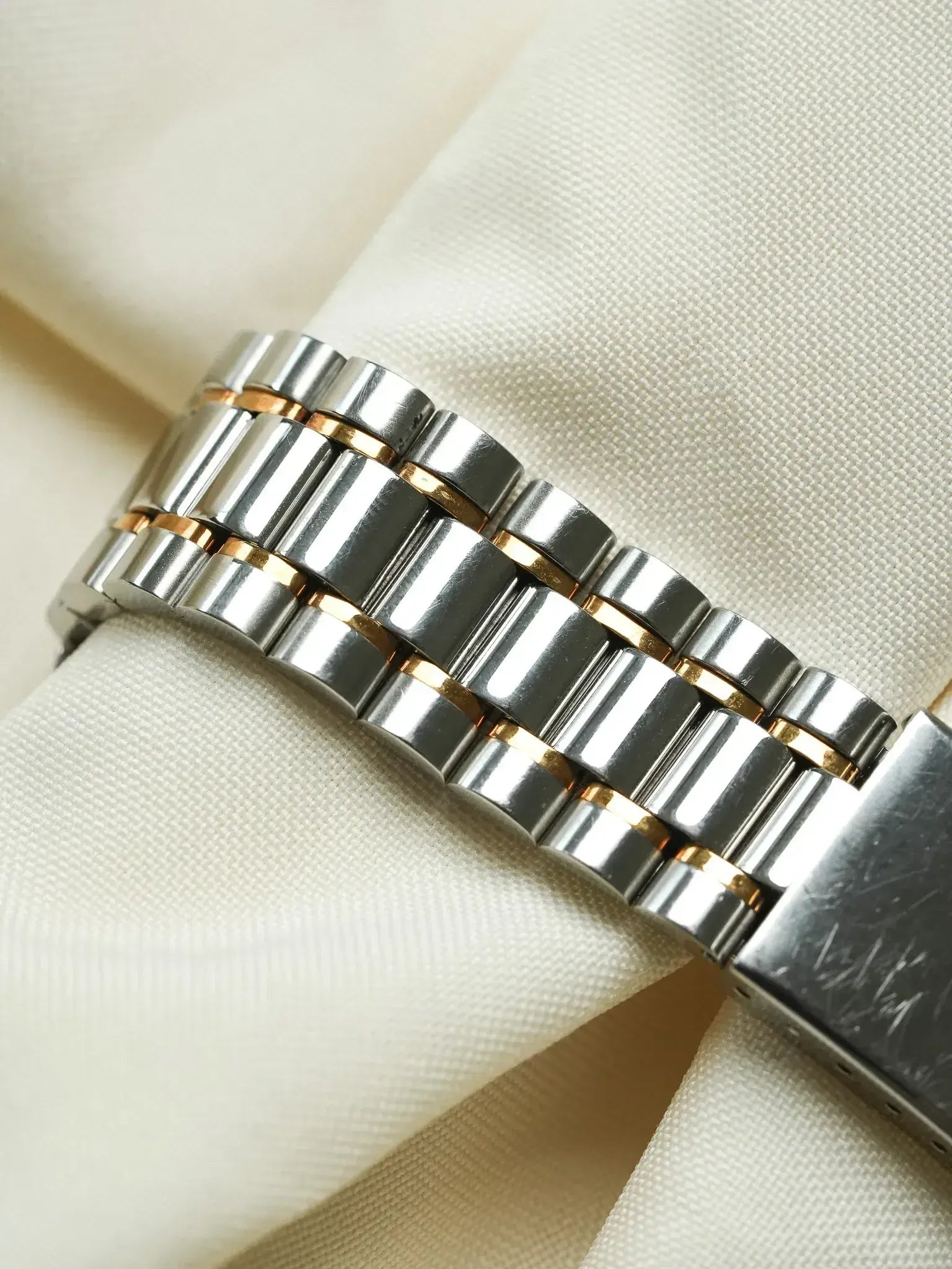 Rolex vintage bracelet in stainless steel and gold, resting on cream fabric