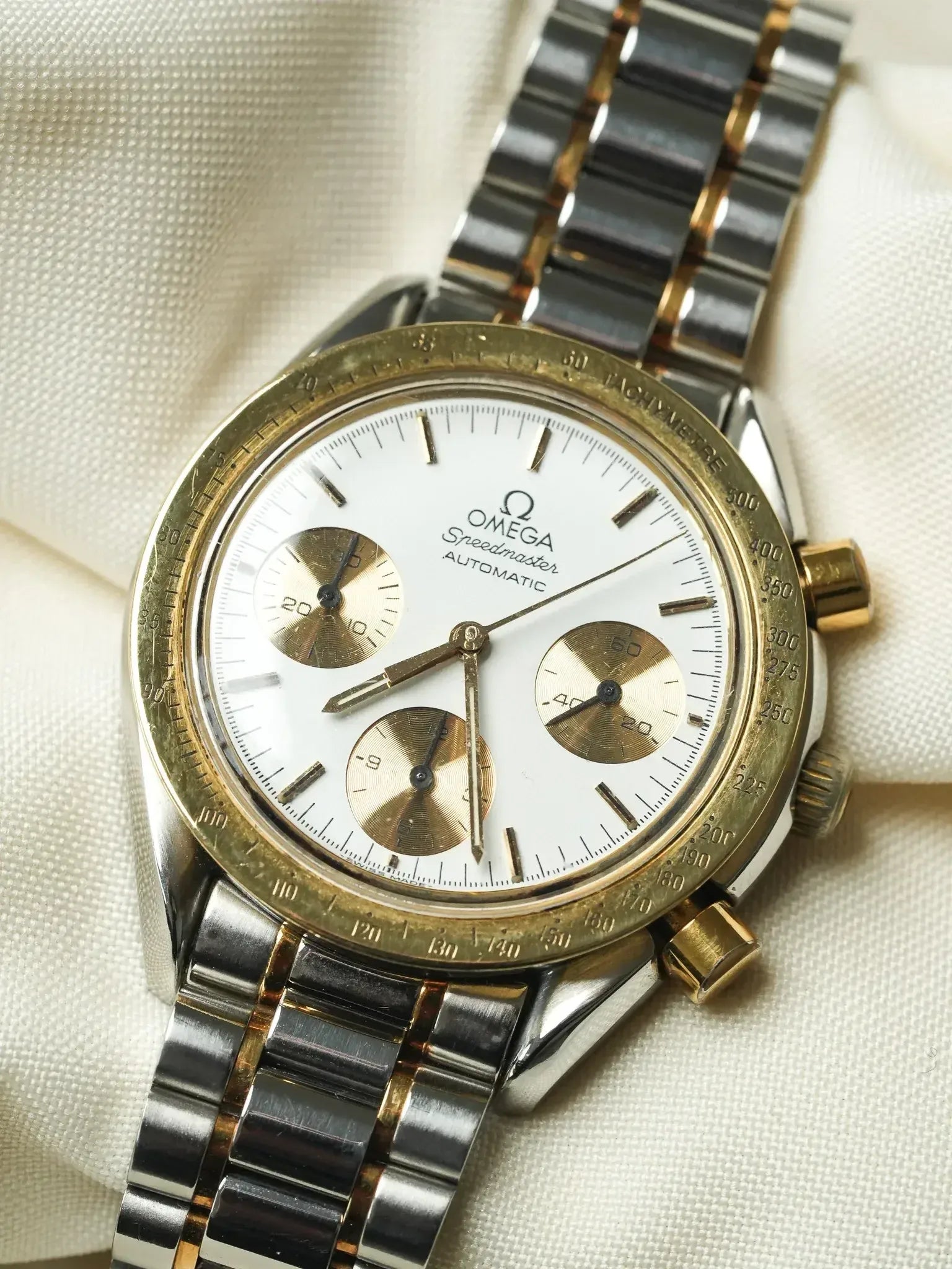 Omega Speedmaster vintage chronograph with white dial, gold subdials, and two-tone bracelet