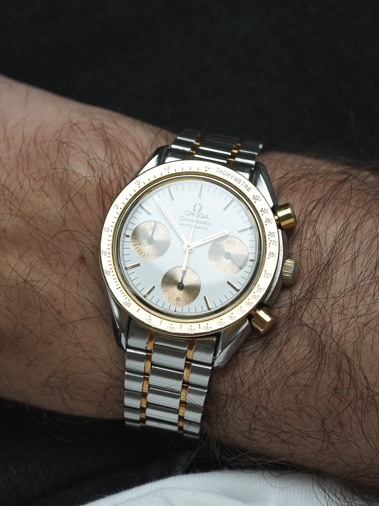 Omega Speedmaster vintage chronograph with silver dial, gold bezel, and two-tone bracelet on wrist