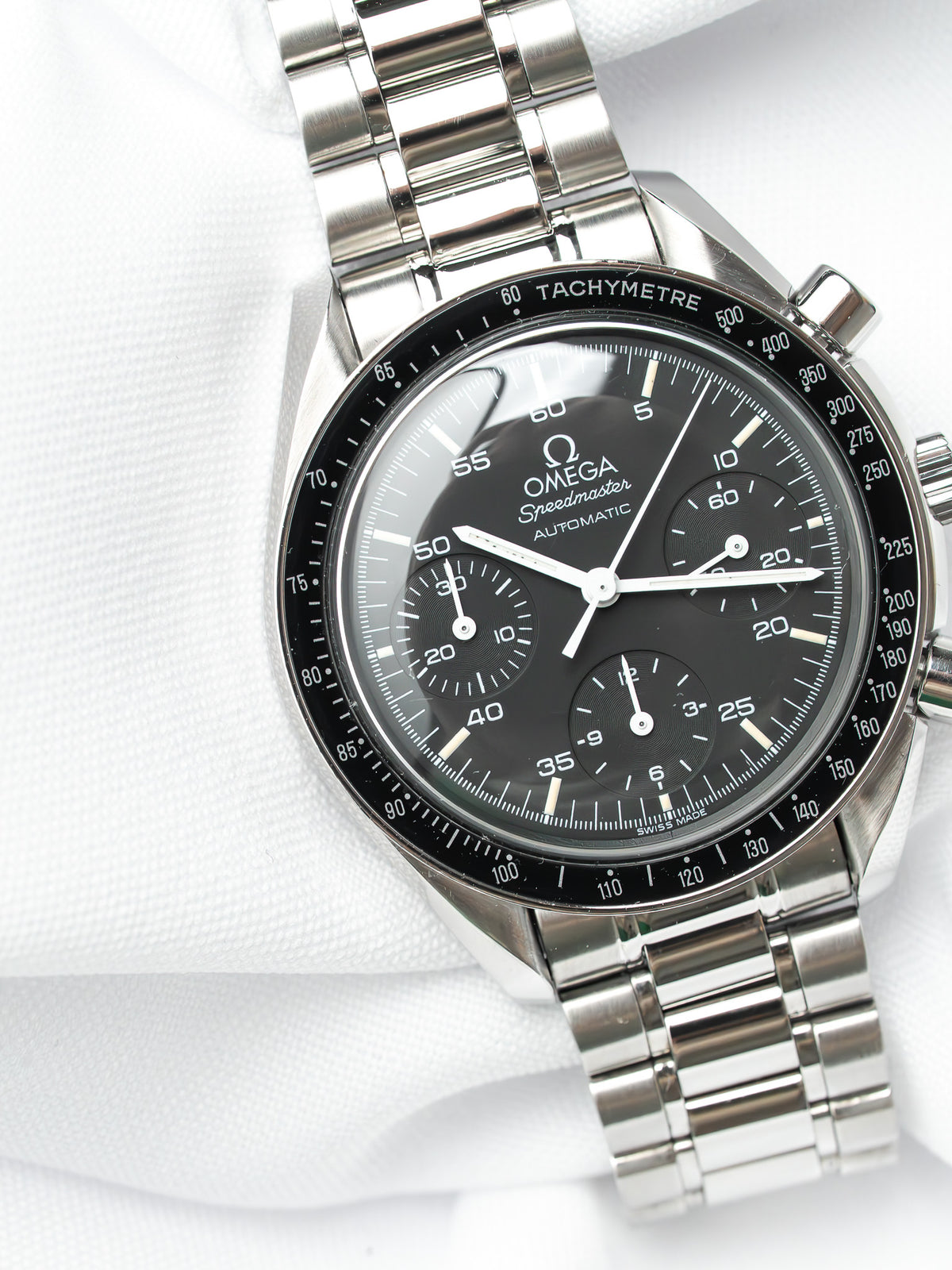Omega Speedmaster Automatic chronograph with black dial, steel bracelet, tachymeter bezel on white fabric