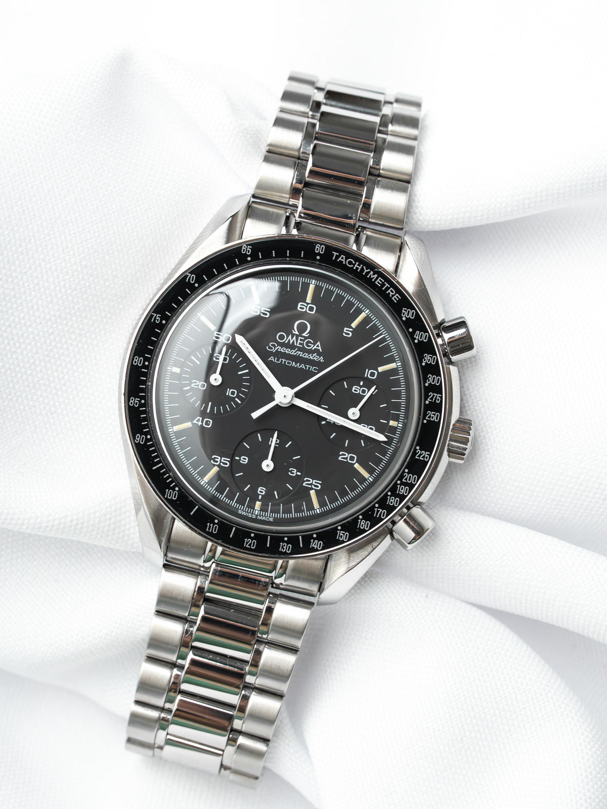 Omega Speedmaster Automatic vintage watch with black dial, steel bracelet, tachymeter bezel on white fabric