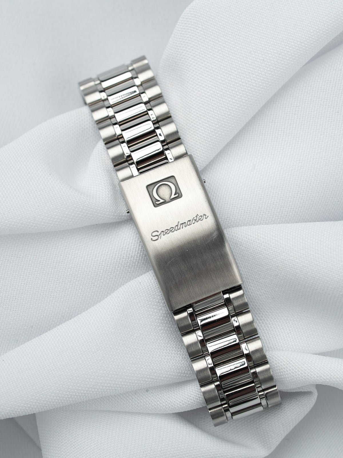 Omega Speedmaster vintage bracelet en acier, fermoir gravé, posé sur tissu blanc