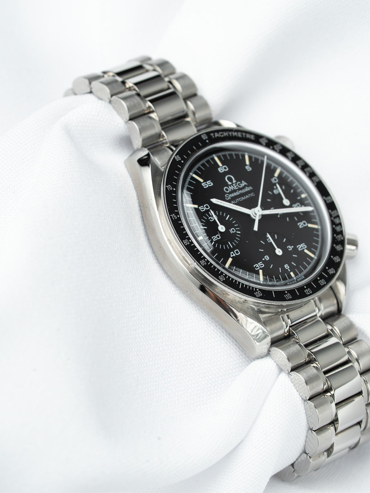 Omega Speedmaster vintage chronograph with black dial, steel bracelet, tachymeter bezel on white fabric