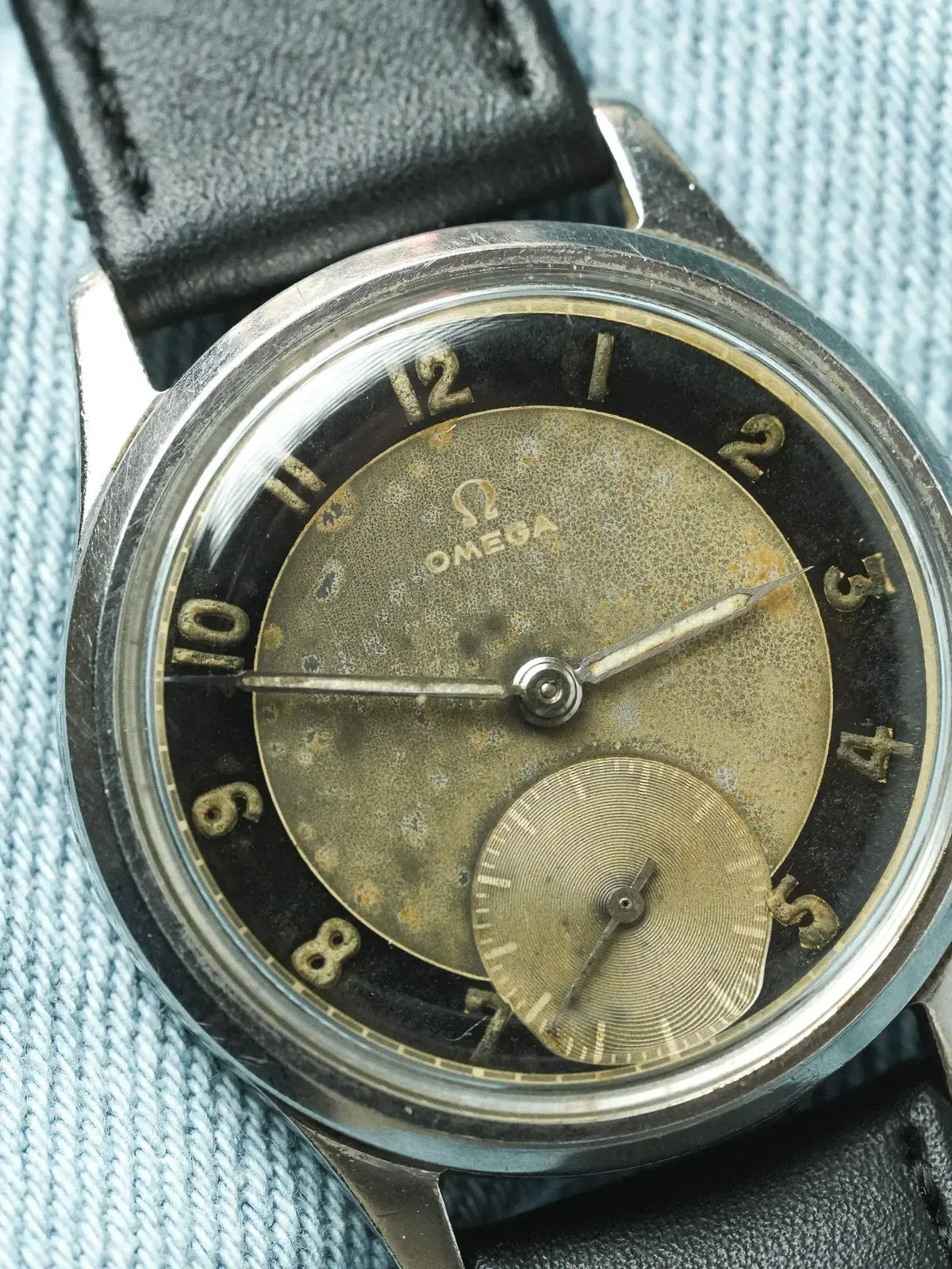 Vintage Omega wristwatch with aged dial, black leather strap, and steel case