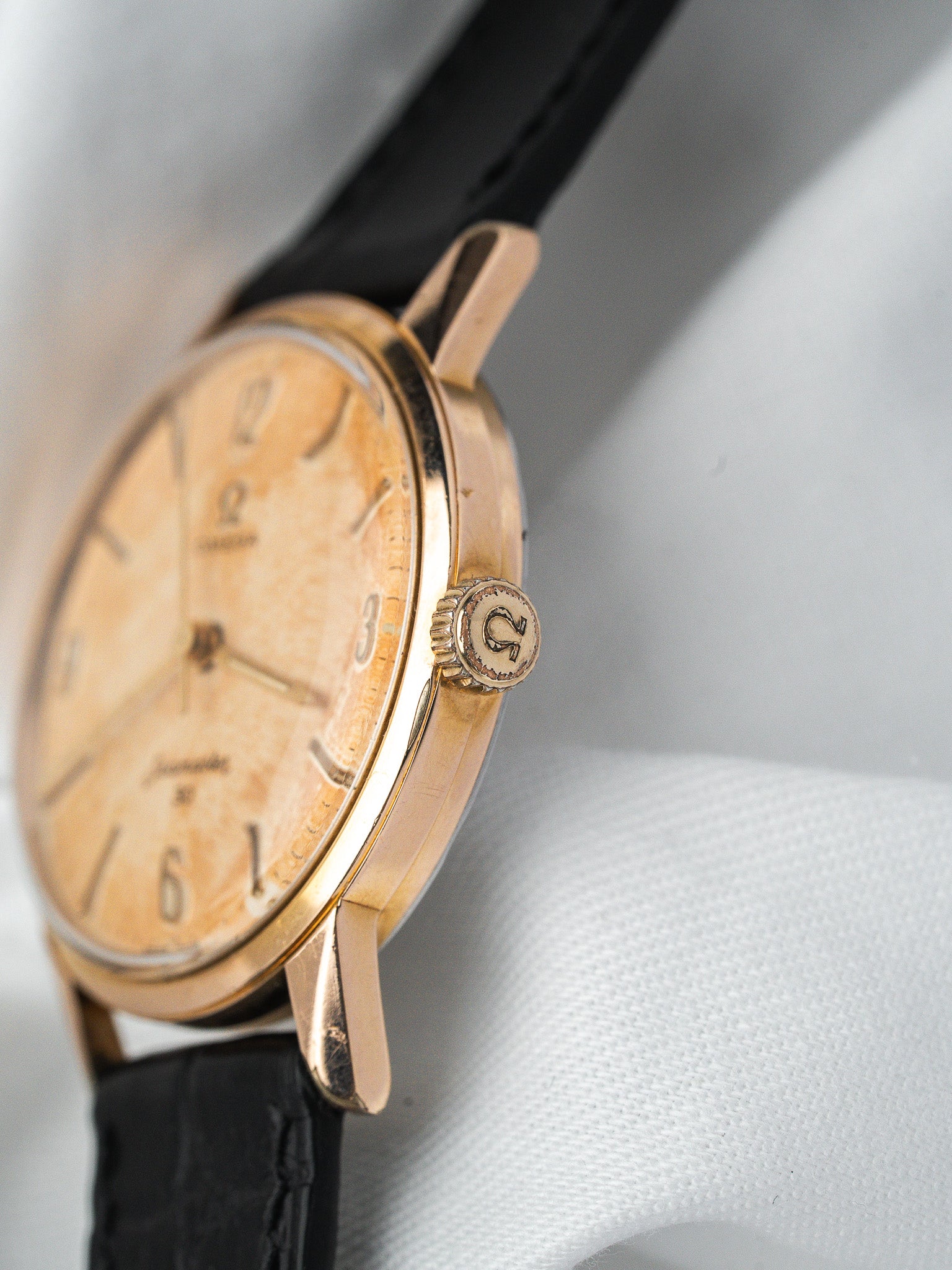 Vintage Omega watch with gold case, cream dial, black leather strap on white background