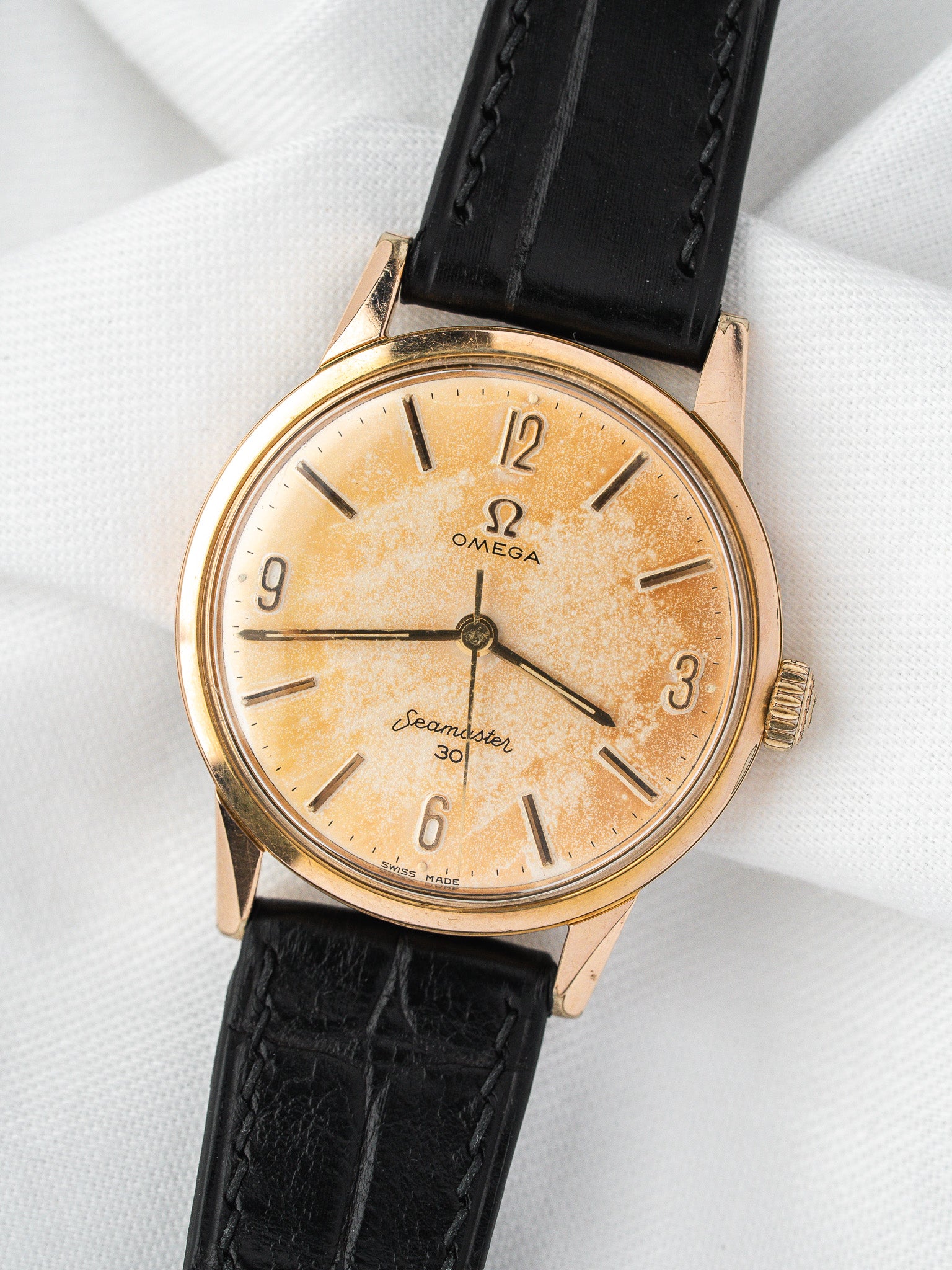Vintage Omega Seamaster 30 watch with gold case, aged dial, black leather strap on white fabric
