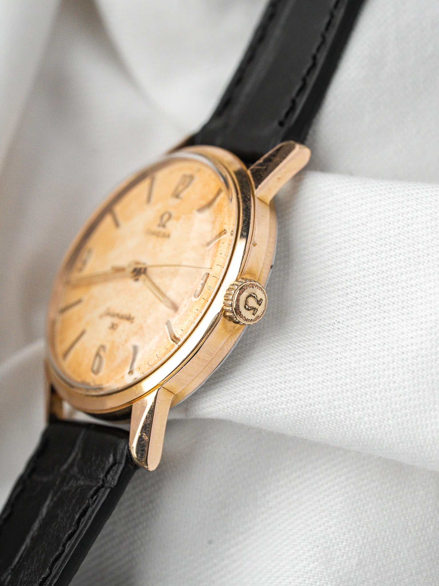Vintage Omega watch with gold case, cream dial, black leather strap on white fabric