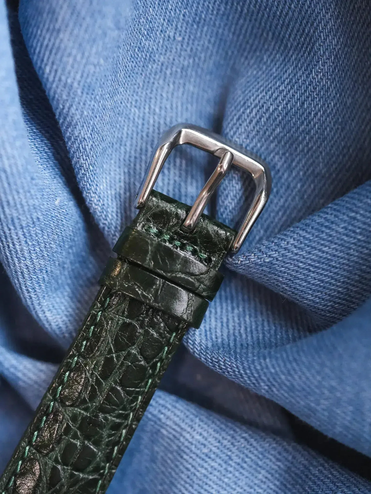 Green alligator leather watch strap with silver buckle on blue denim