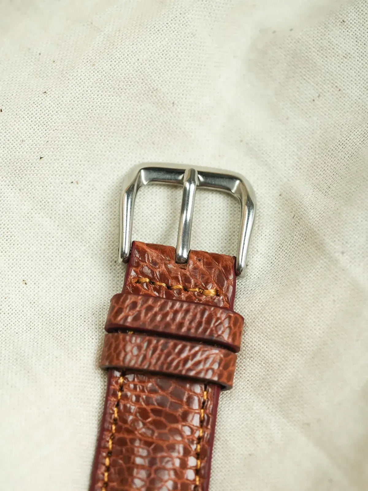 Brown textured leather watch strap with silver buckle and gold stitching