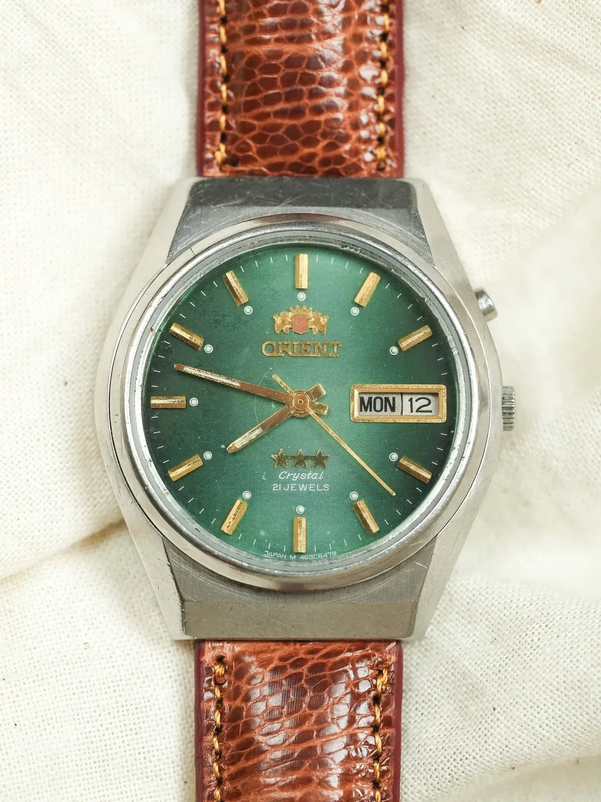Orient vintage watch with green dial, gold markers, brown leather strap on fabric