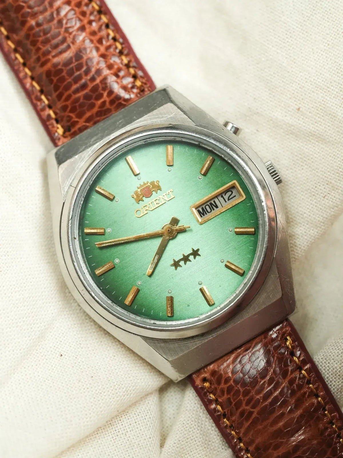Orient vintage watch with green dial, gold markers, brown leather strap on fabric