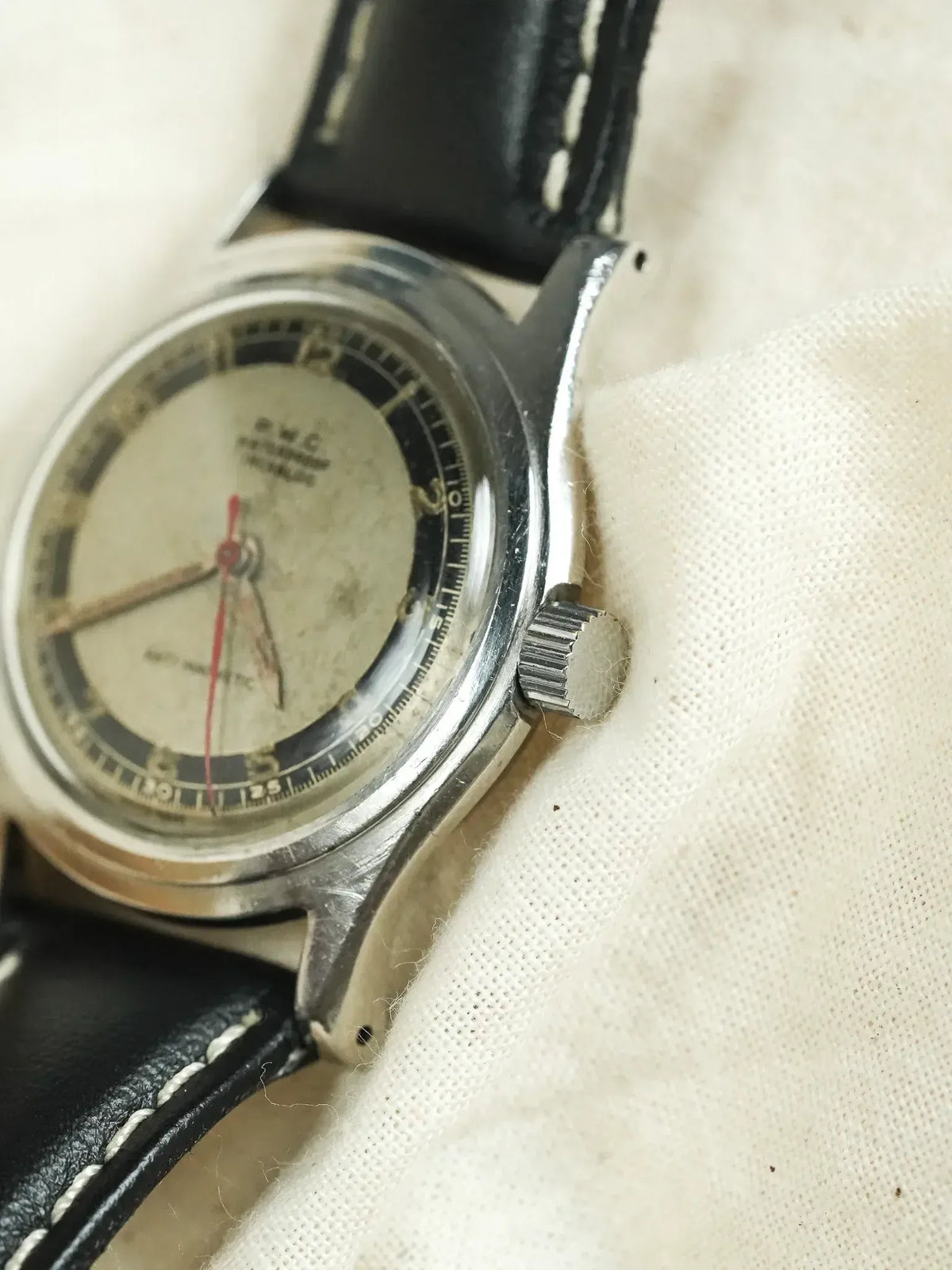 Vintage Universal Genève automatic watch with silver dial, black leather strap, on fabric background