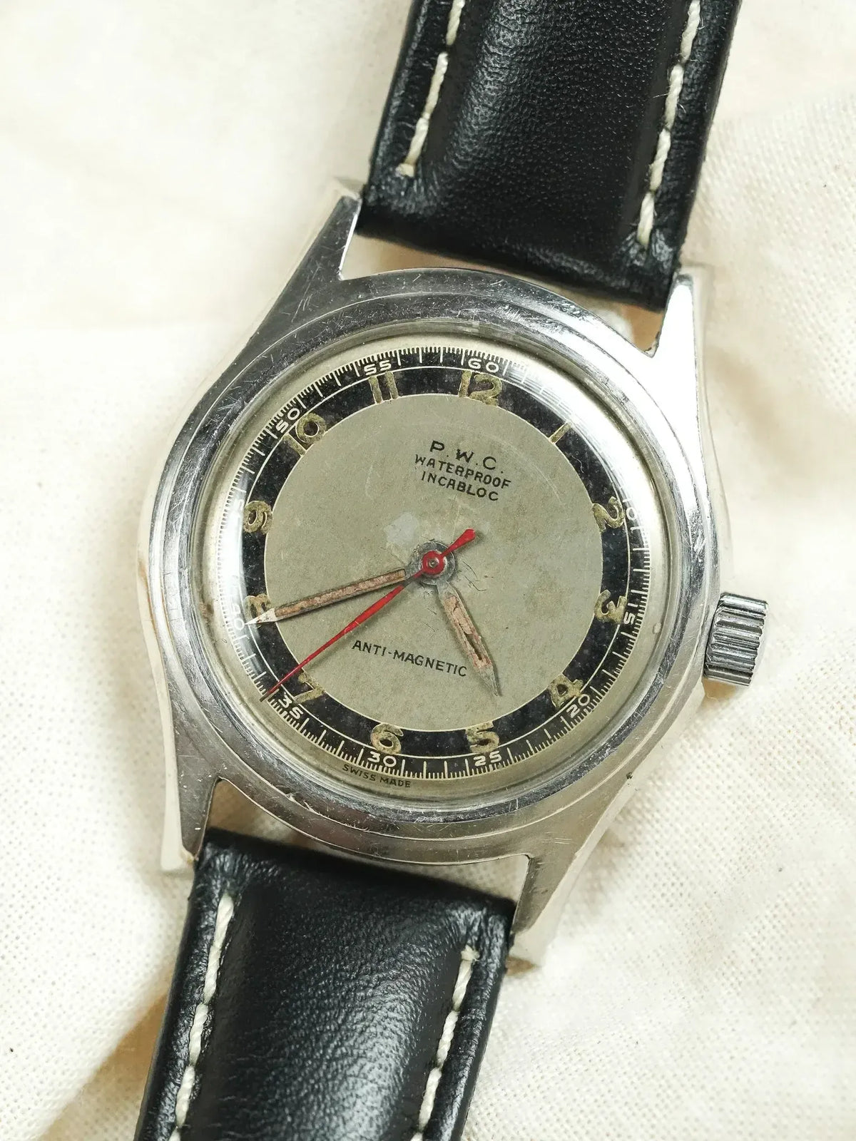 P.W.C. vintage watch with silver dial, black bezel, and black leather strap