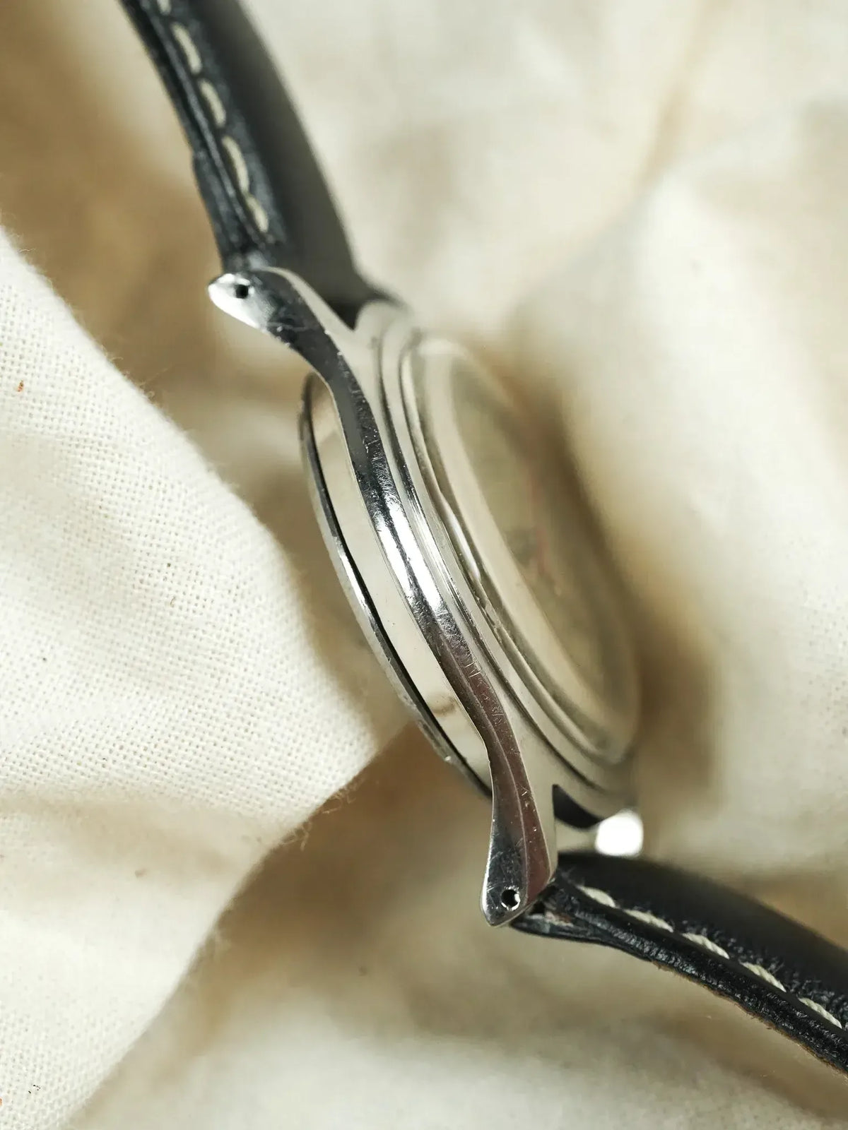Vintage Omega Seamaster watch side view, stainless steel case, black leather strap with white stitching