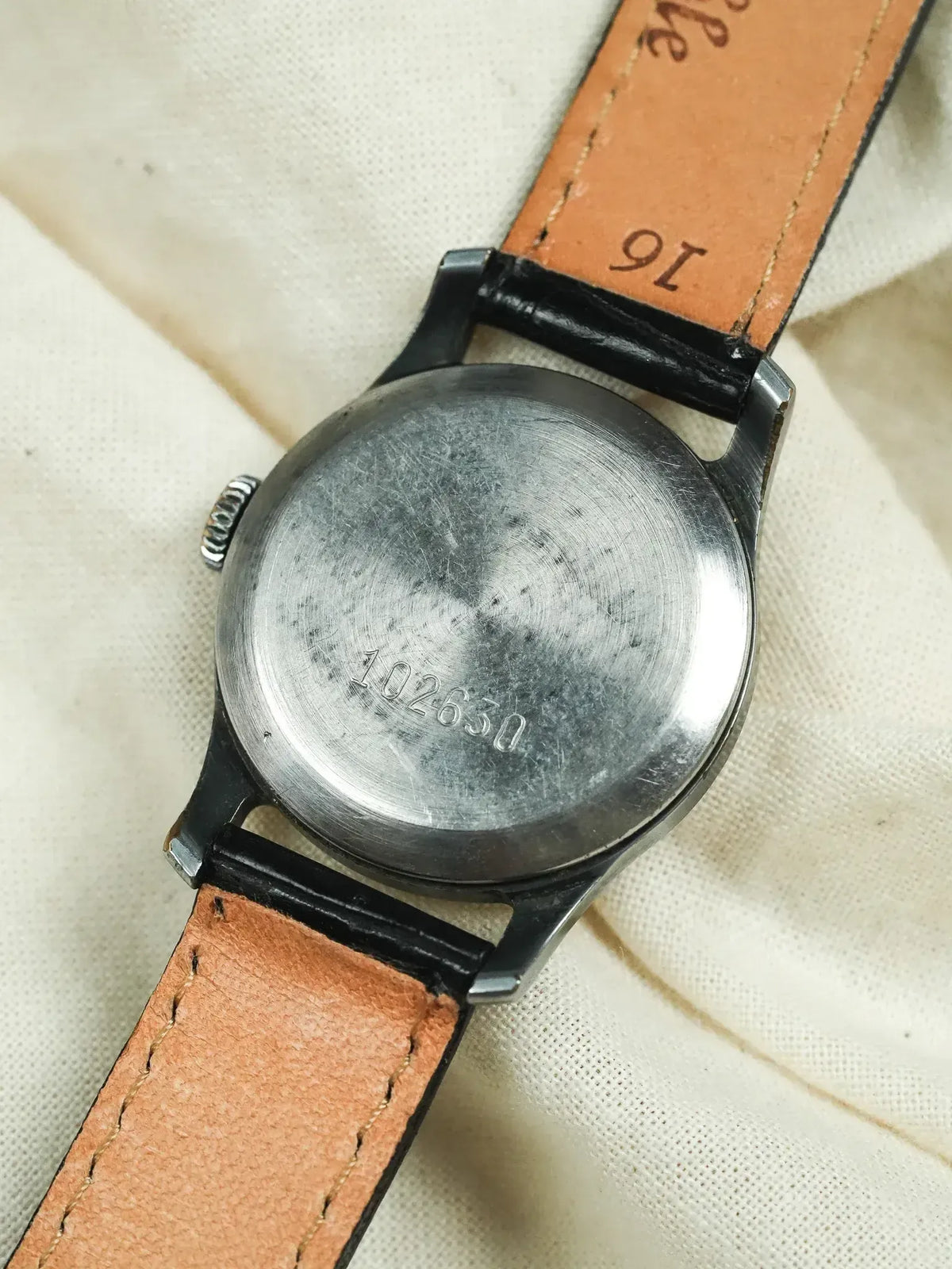 Vintage watch with brushed steel case back, engraved number, tan leather strap on fabric
