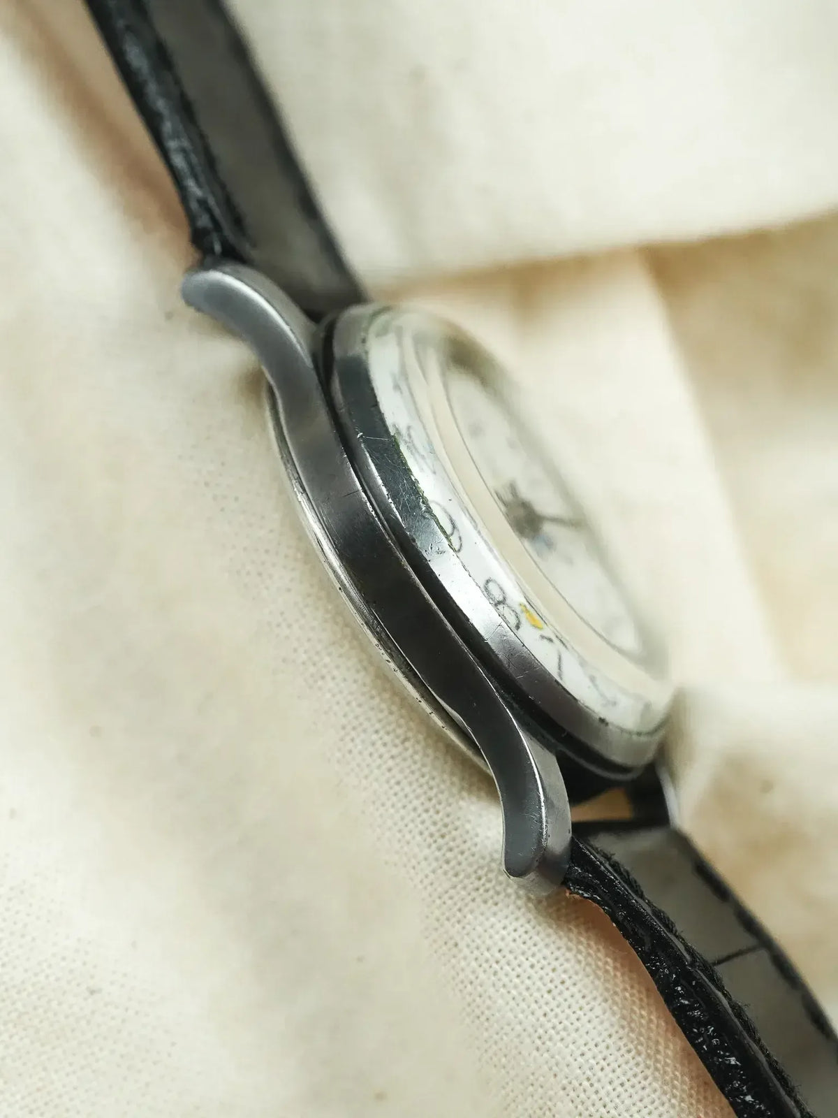 Vintage Omega watch with steel case, white dial, black leather strap on fabric