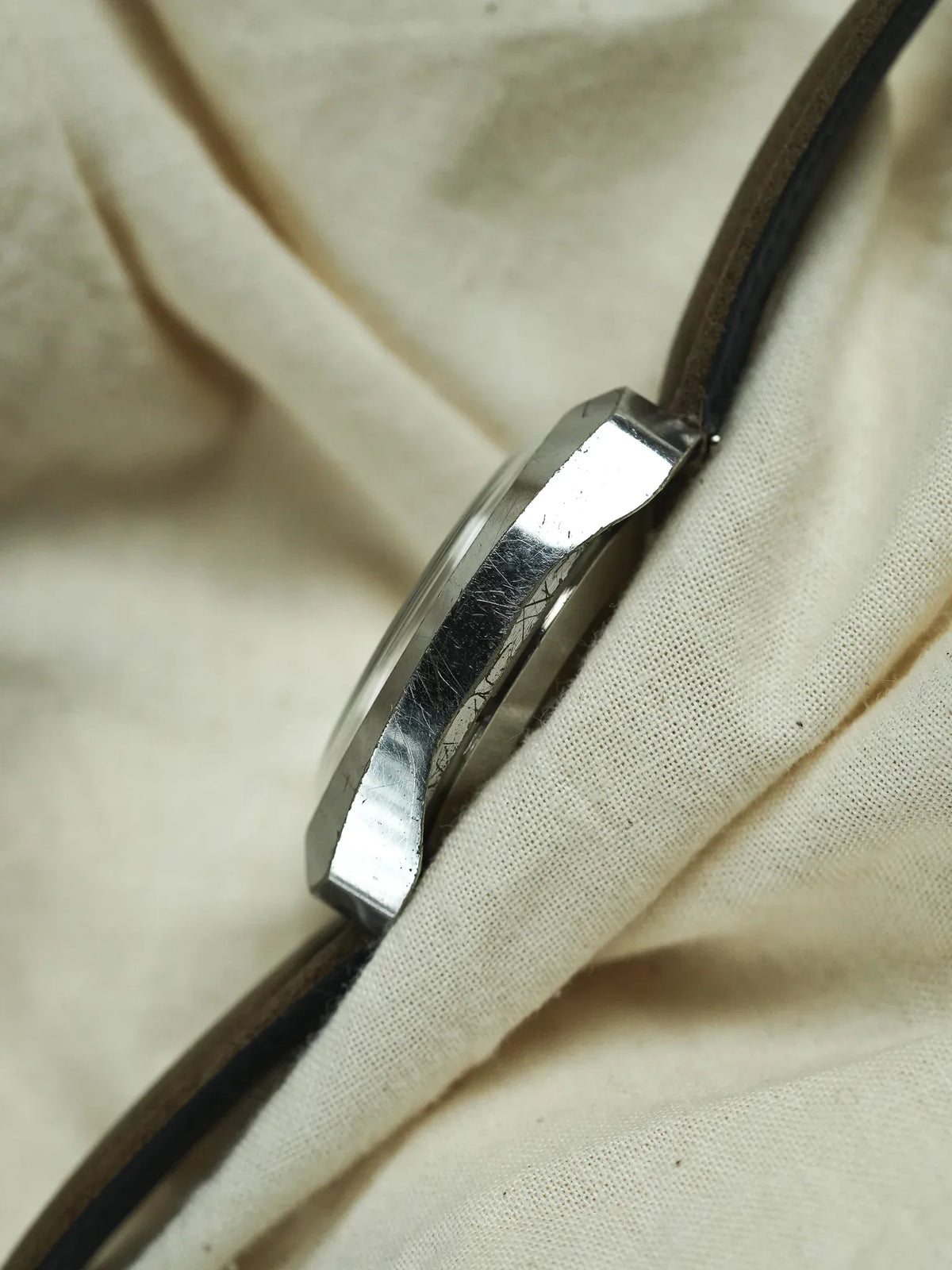 Vintage watch with polished steel case and black leather strap on fabric