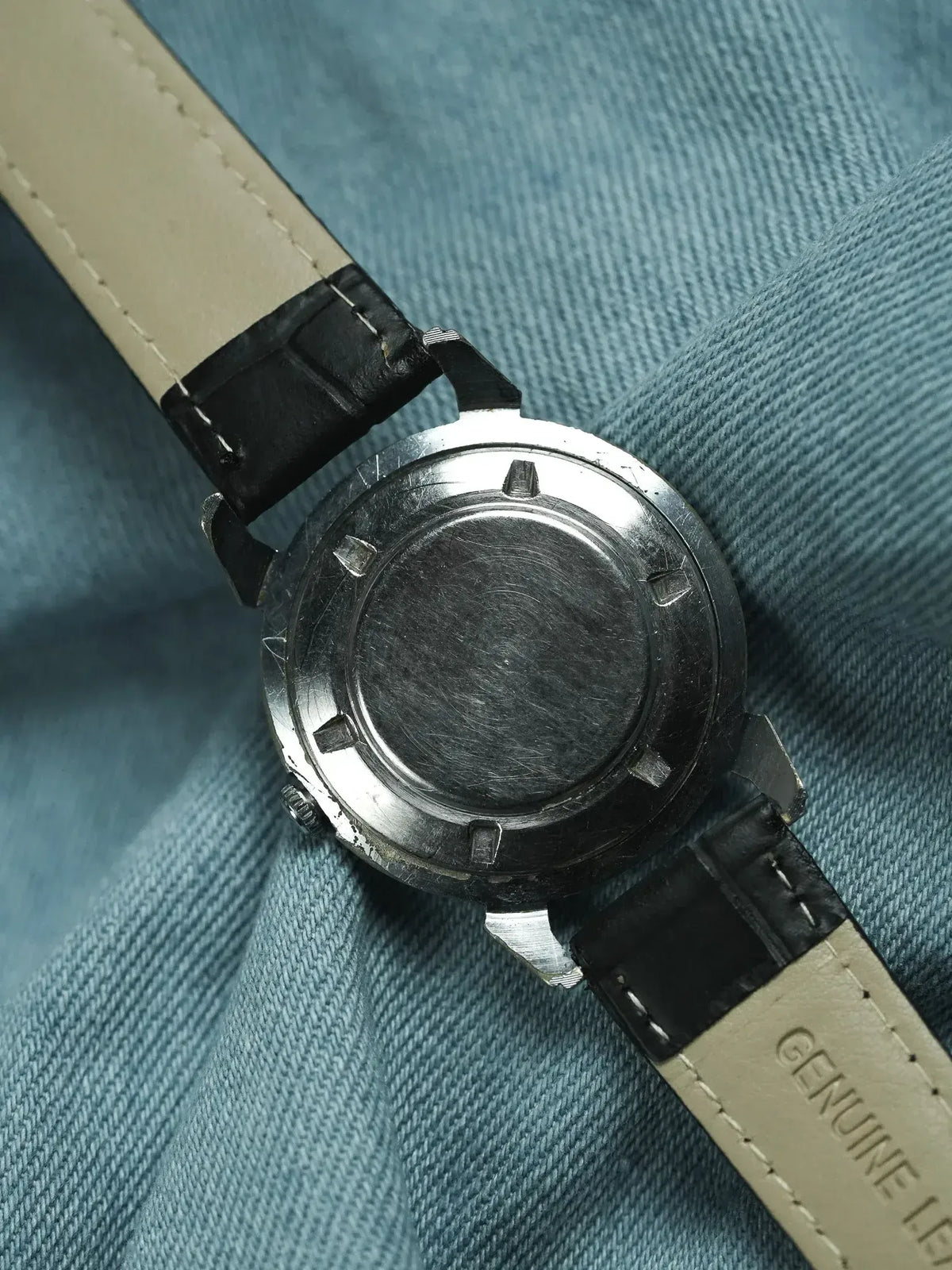 Vintage watch with steel case back and black leather strap on denim