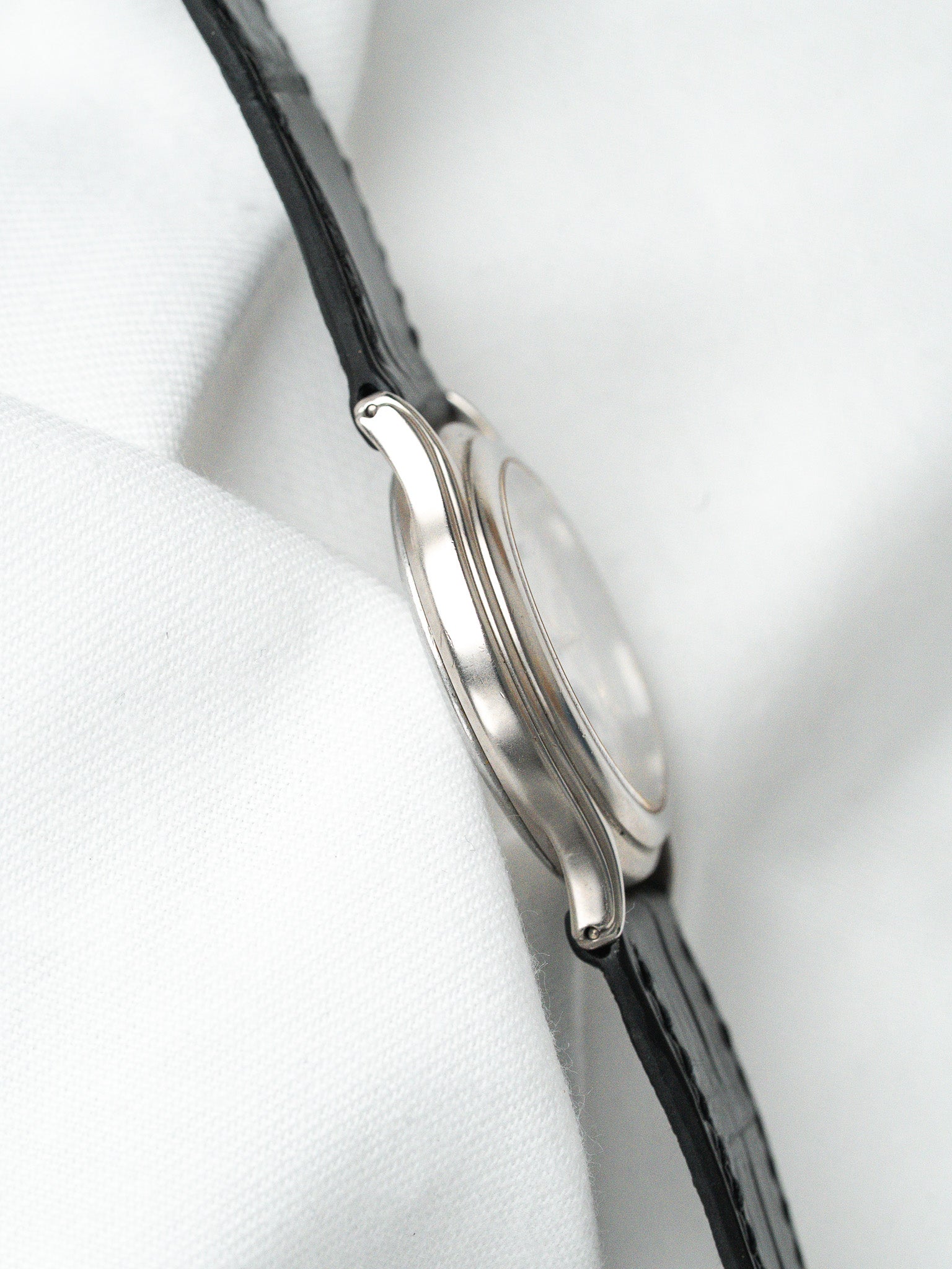 Vintage Cartier watch with silver case and black leather strap on white fabric