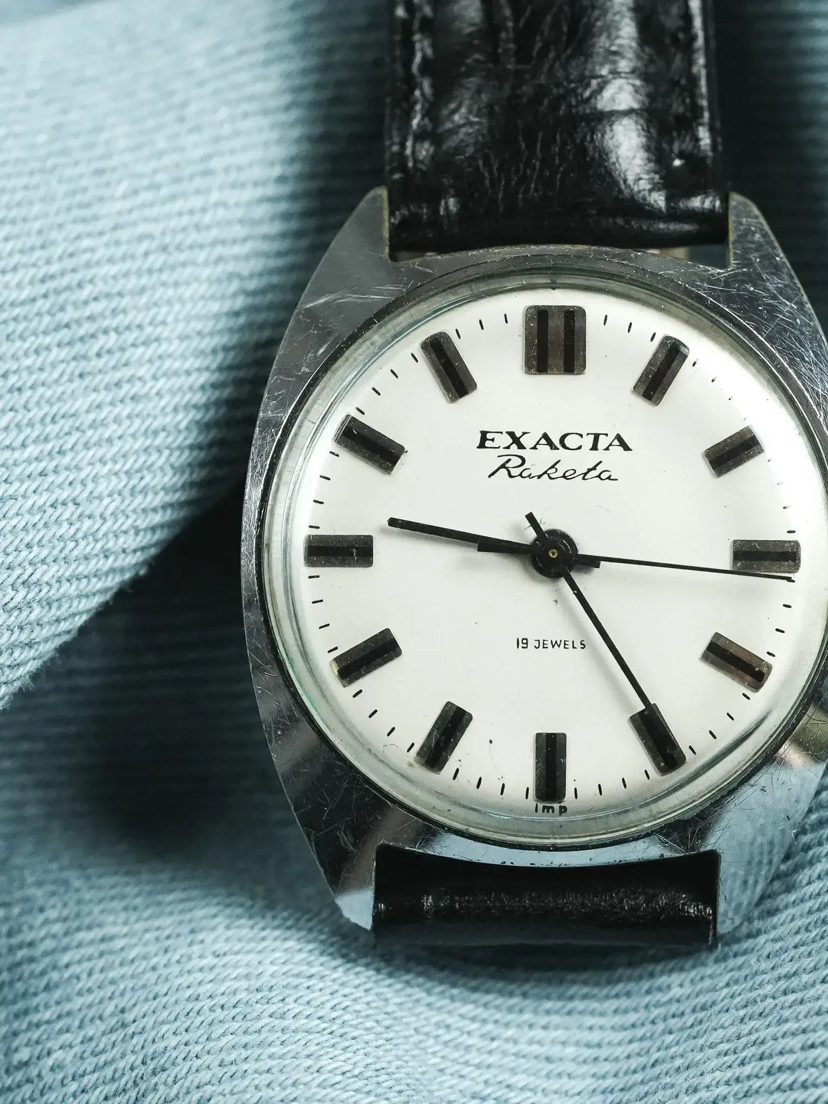 Exacta Raketa vintage watch with white dial, black markers, and leather strap on denim