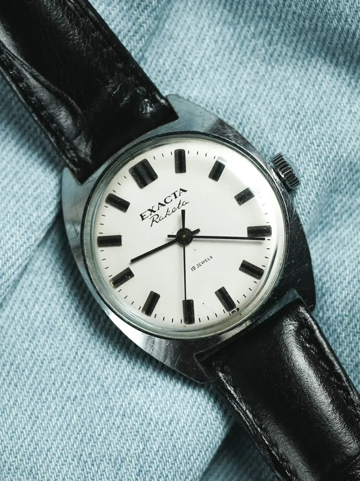 Exacta Raketa vintage watch with white dial, black markers, and black leather strap on denim