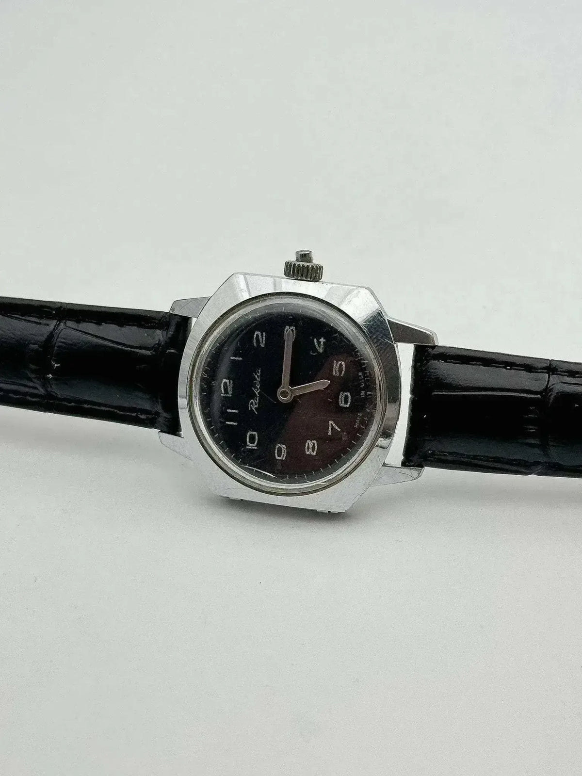 Rolex vintage watch with black dial, steel case, and black leather strap on white background