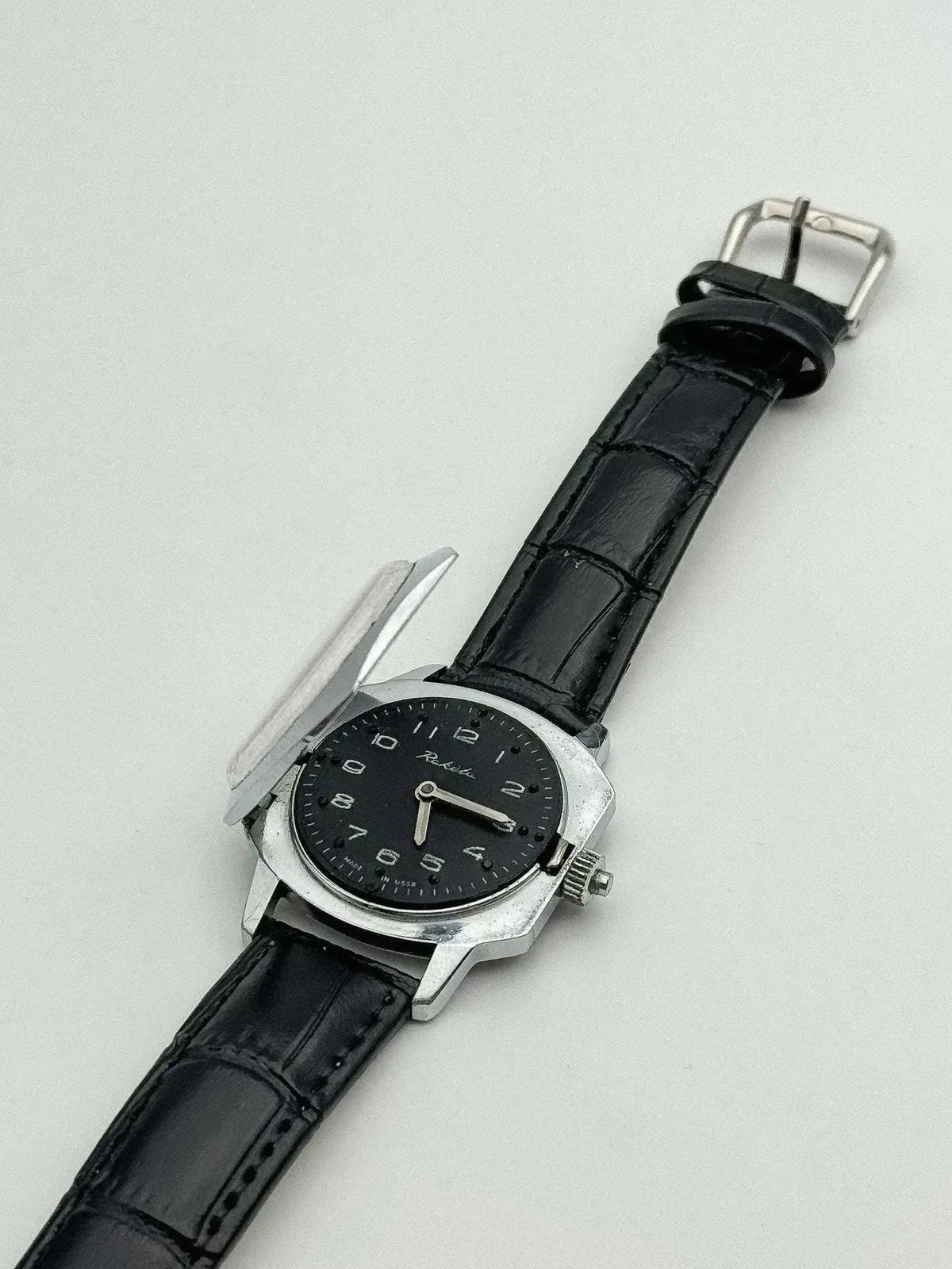 Raketa vintage watch with black dial, steel case, and black leather strap on white background