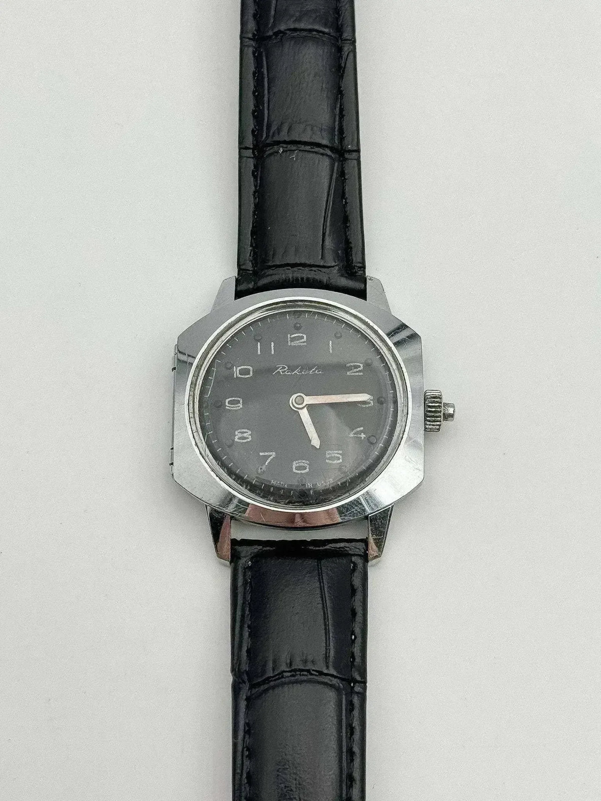Vintage Raketa watch with grey dial, steel case, black leather strap on white background