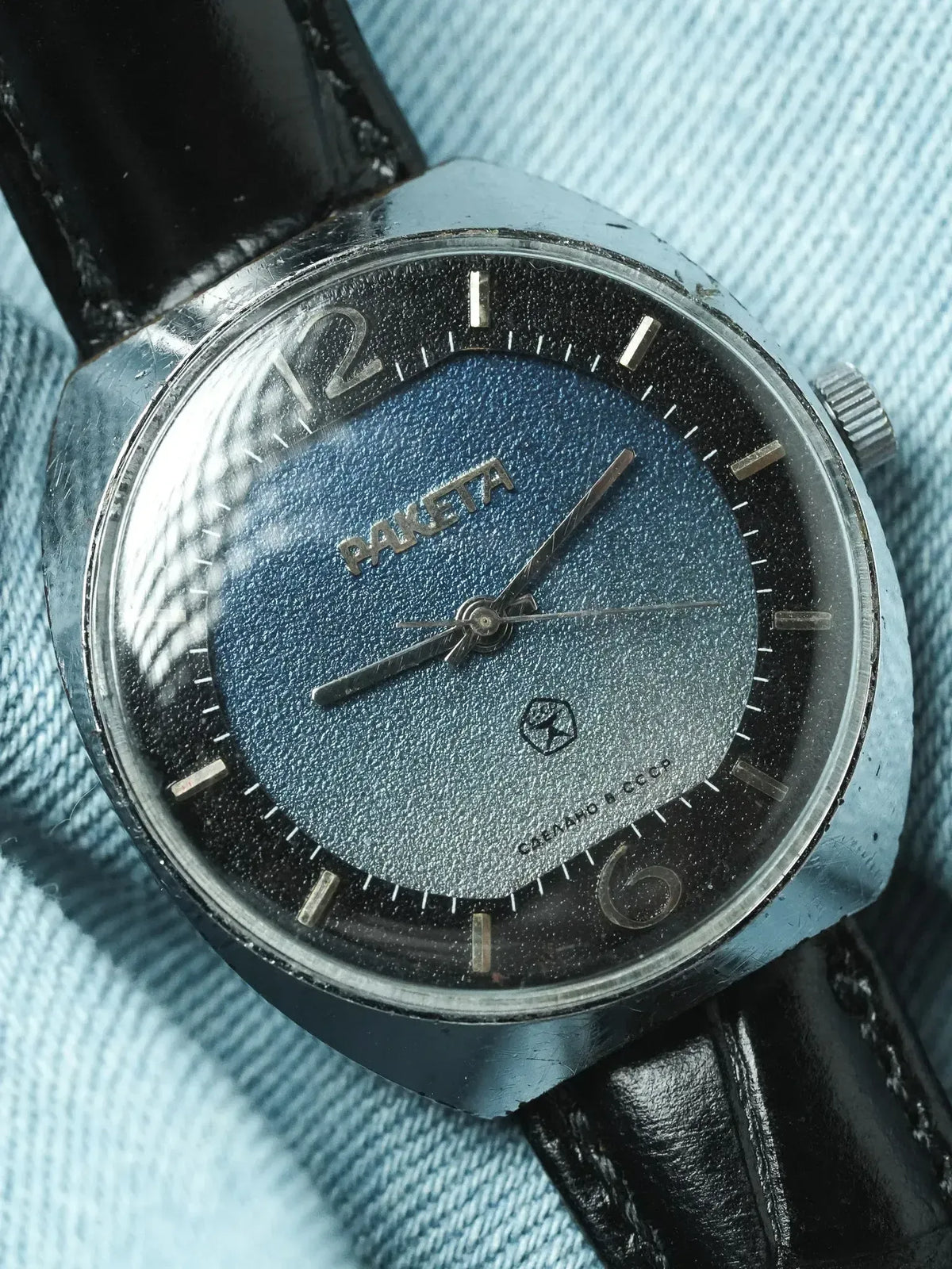 Raketa vintage watch with blue textured dial, black leather strap, on denim background