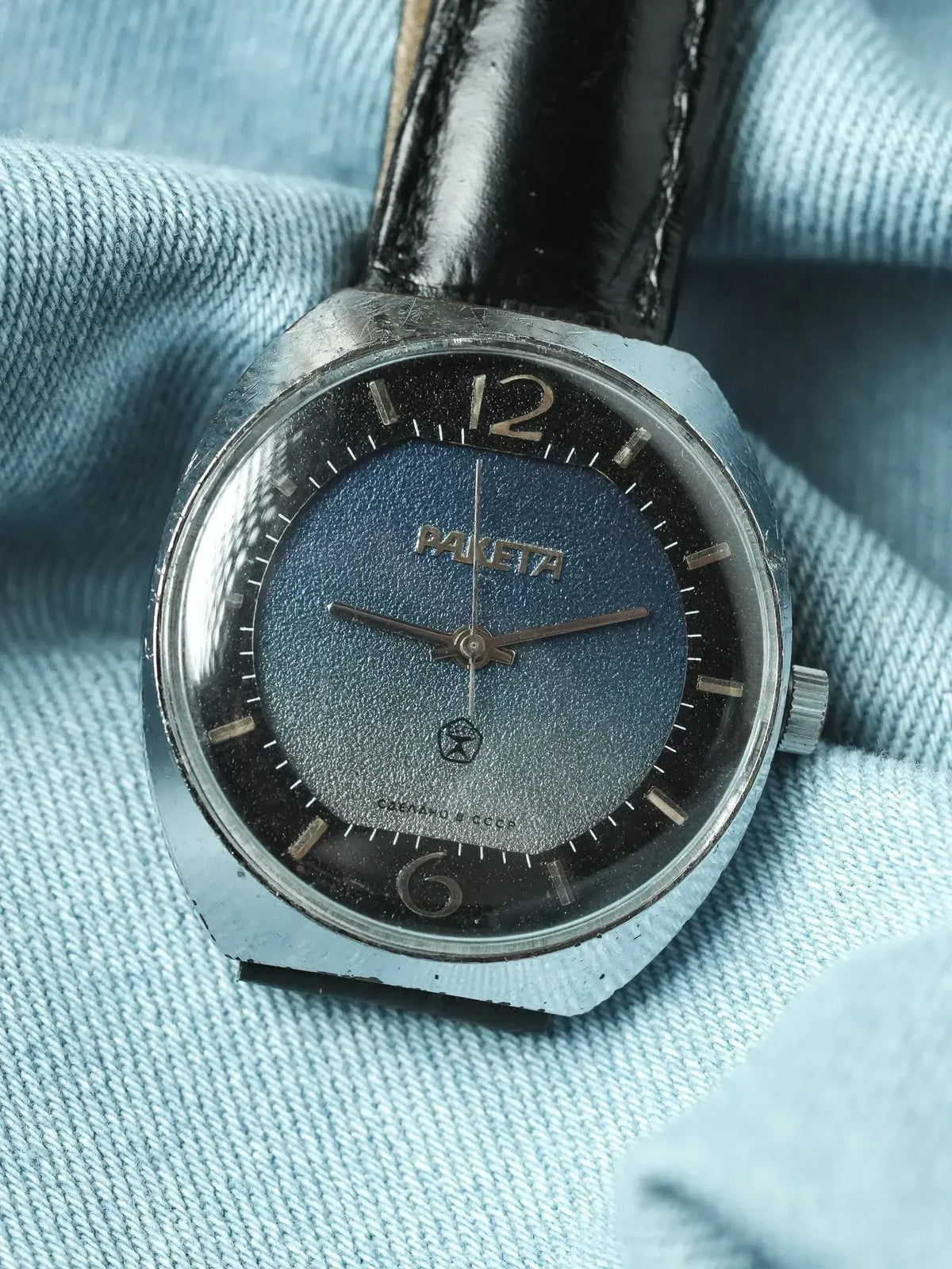 Vintage Raketa watch with blue textured dial, steel case, black leather strap on denim