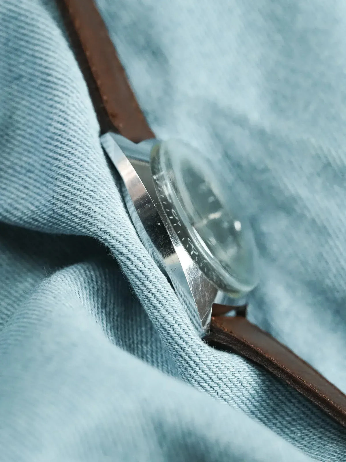 Vintage Rolex watch with stainless steel case and brown leather strap on denim